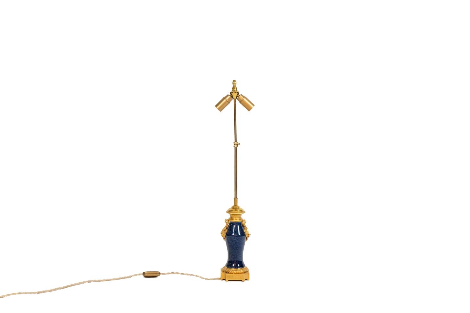 Lampe de table en porcelaine bleue et sertie de bronze doré, ornée de feuilles de vigne au sommet du corps, le haut du cadre orné d'une grille régulière et le pied de la base décoré de feuilles. Base quadripode avec forme incurvée aux angles et
