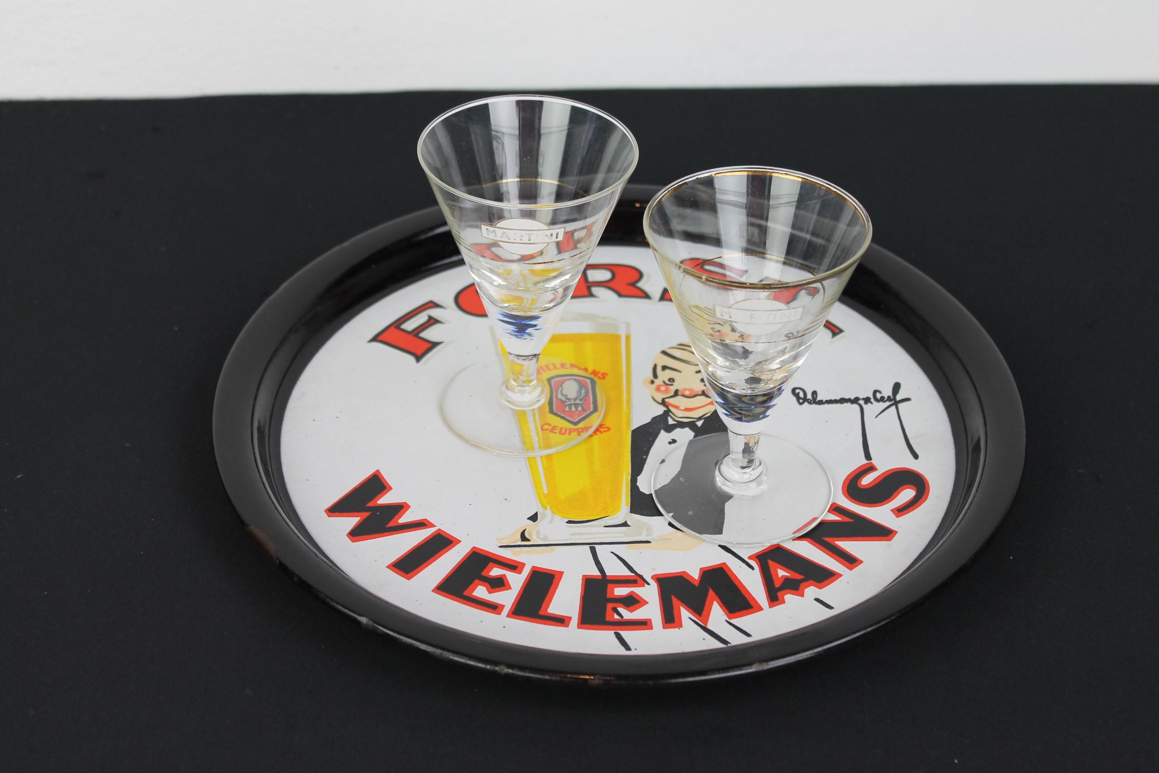 Porcelain tray for the Belgian Brewery Wielemans - Ceuppens which was located in Brussels, Belgium. 
This beer tray has a great design: a waiter serving a giant glass of blond Wielemans - Ceuppens beer which was done by Delamare & Cerf. The enamel