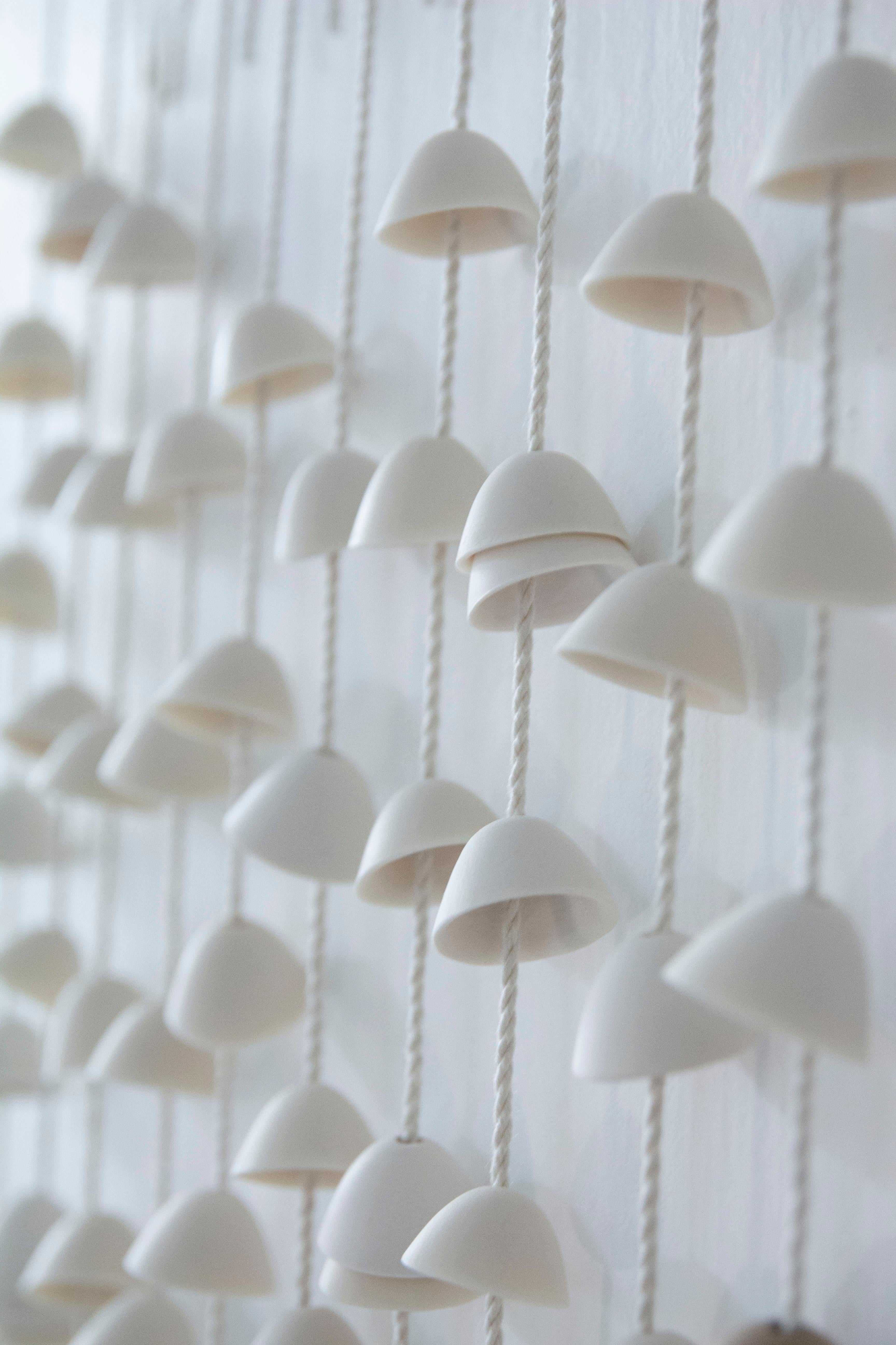 Oggetto da appendere in porcellana realizzato a mano dall'artista Kristina Kotlier. Le campane di porcellana sono infilate a mano su una corda di cotone. Sono disponibili misure personalizzate. 