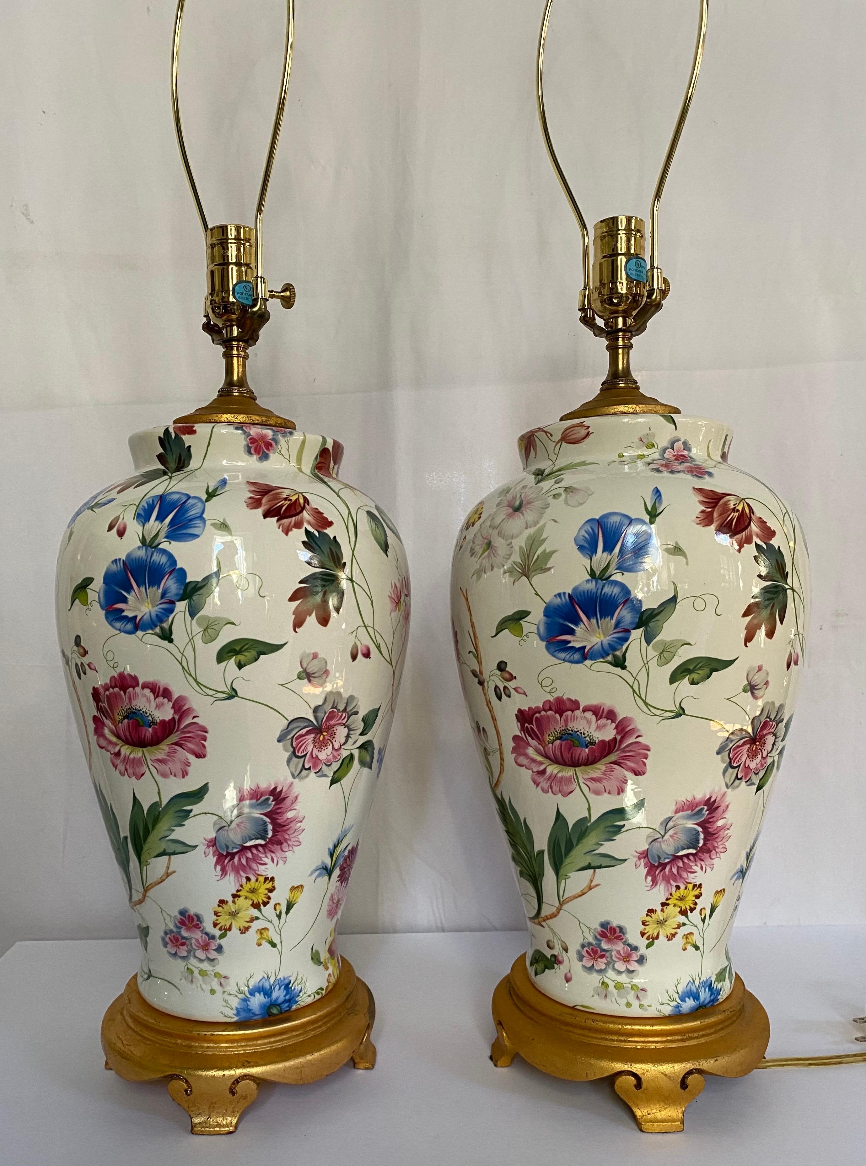 Pair of porcelain botanical table lamps by Chelsea House. These ginger jar urn shaped lamps feature vibrant hand painted floral and vine decorations and are mounted on gilt composite plinth footed bases.  