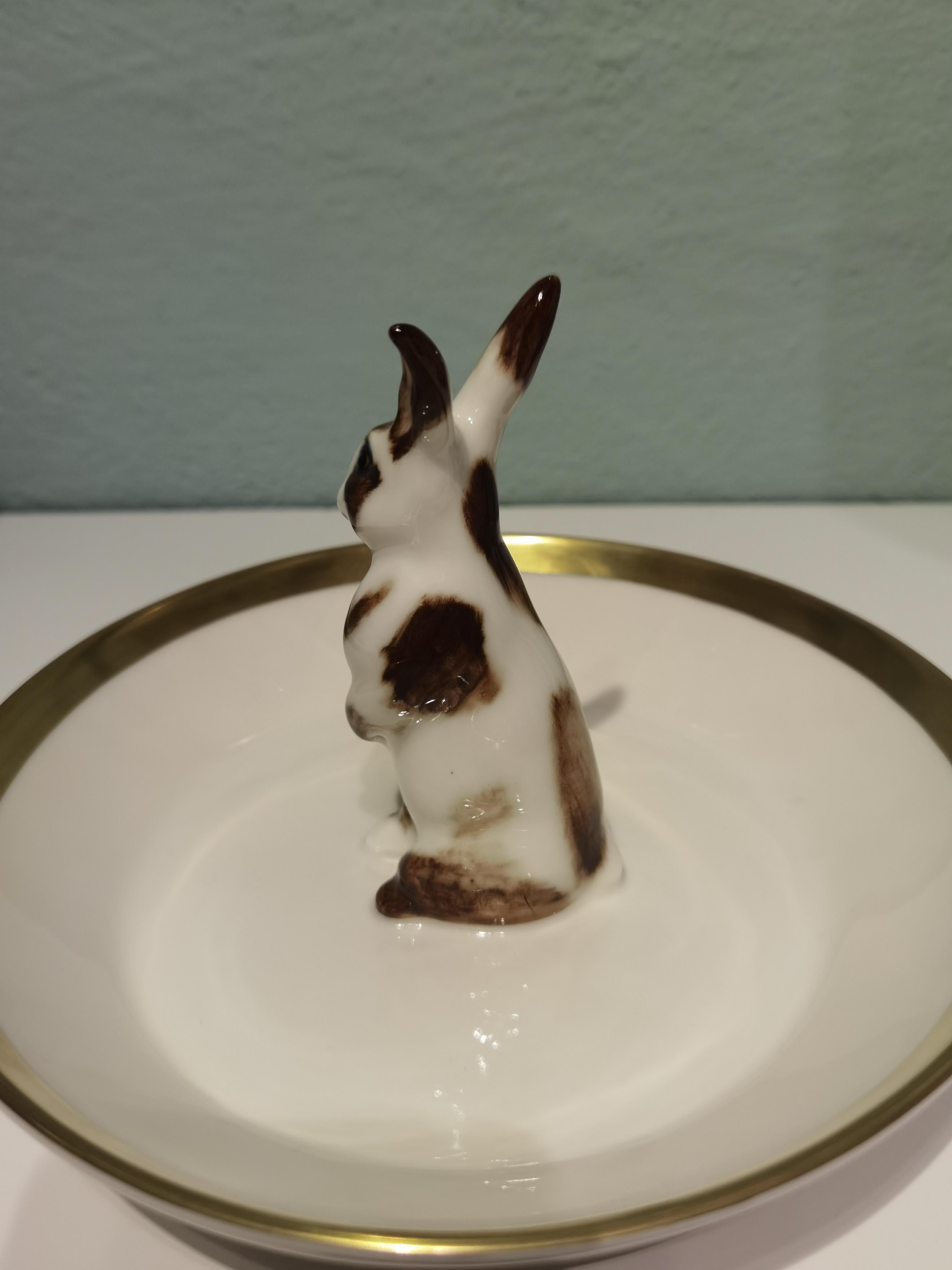 Bol en porcelaine entièrement fabriqué à la main avec un lapin de Pâques peint de façon naturaliste dans des couleurs brunes et blanches. Le lapin est assis au milieu du bol pour décorer les noix ou les bonbons autour de la figure. Il est cerclé