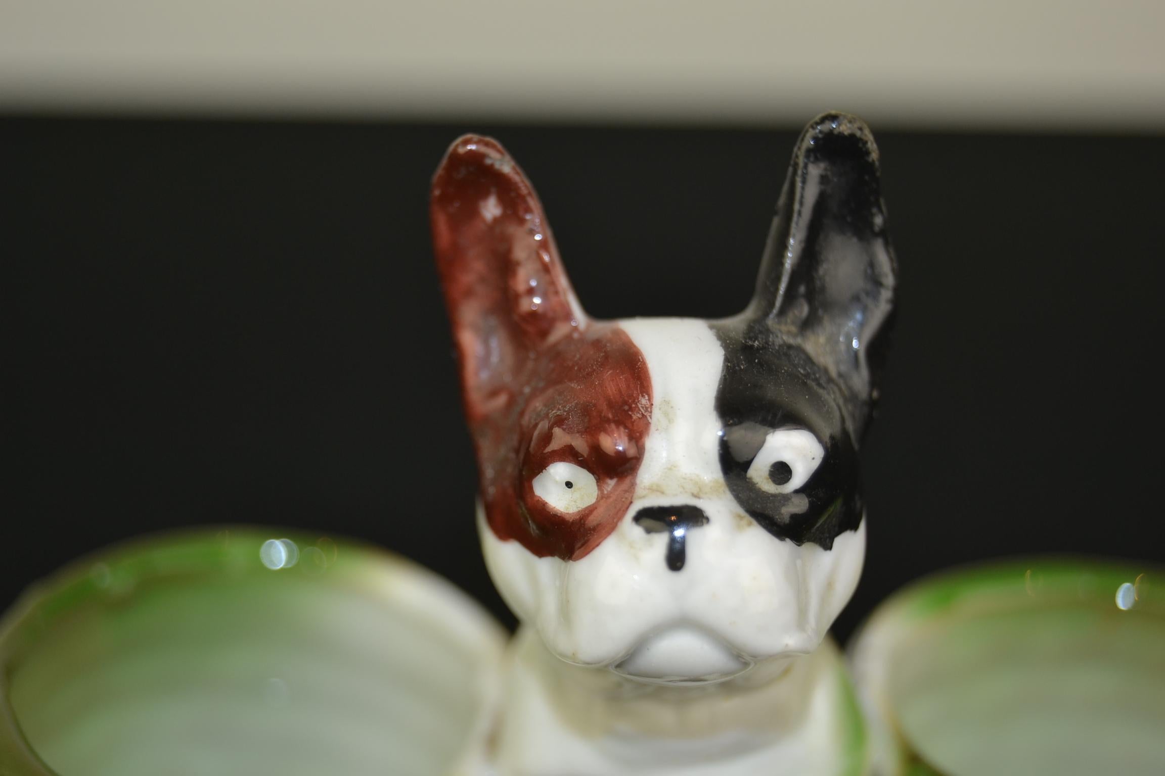 Art Deco porcelain bulldog sculpture. This bulldog sculpture is sitting between two open green baskets which can be used to put mustard, salt or other in. Bulldog figurine has the white color with a brown and black ear. This dog sculpture is in