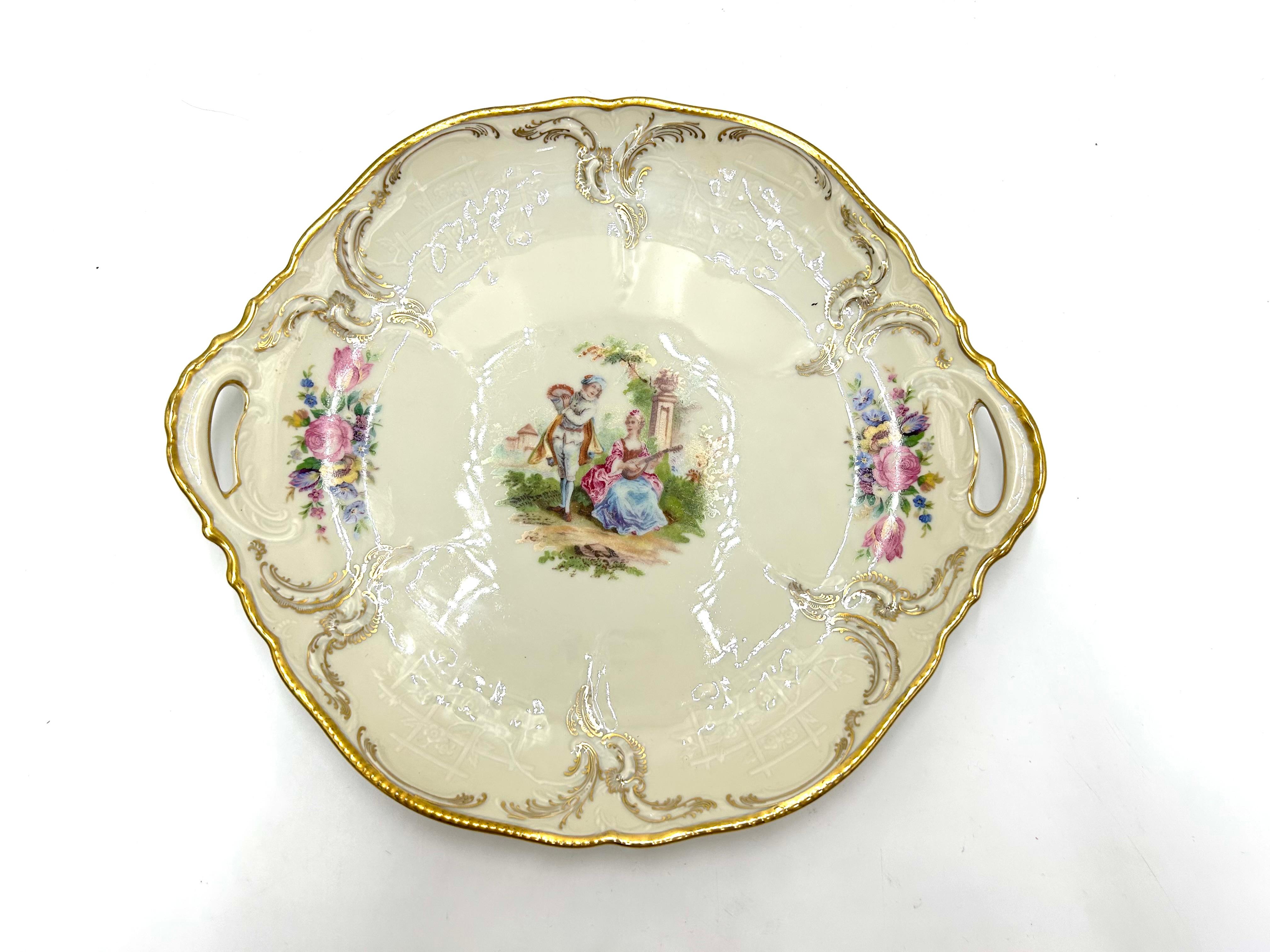 A large porcelain cake dish, a product of the Sanssouci series by the valued German manufacturer Rosenthal.
Porcelain in ecru color, decorated with gilding, motif of floral bouquets and a genre scene.
Signed with the mark of the manufacturer from