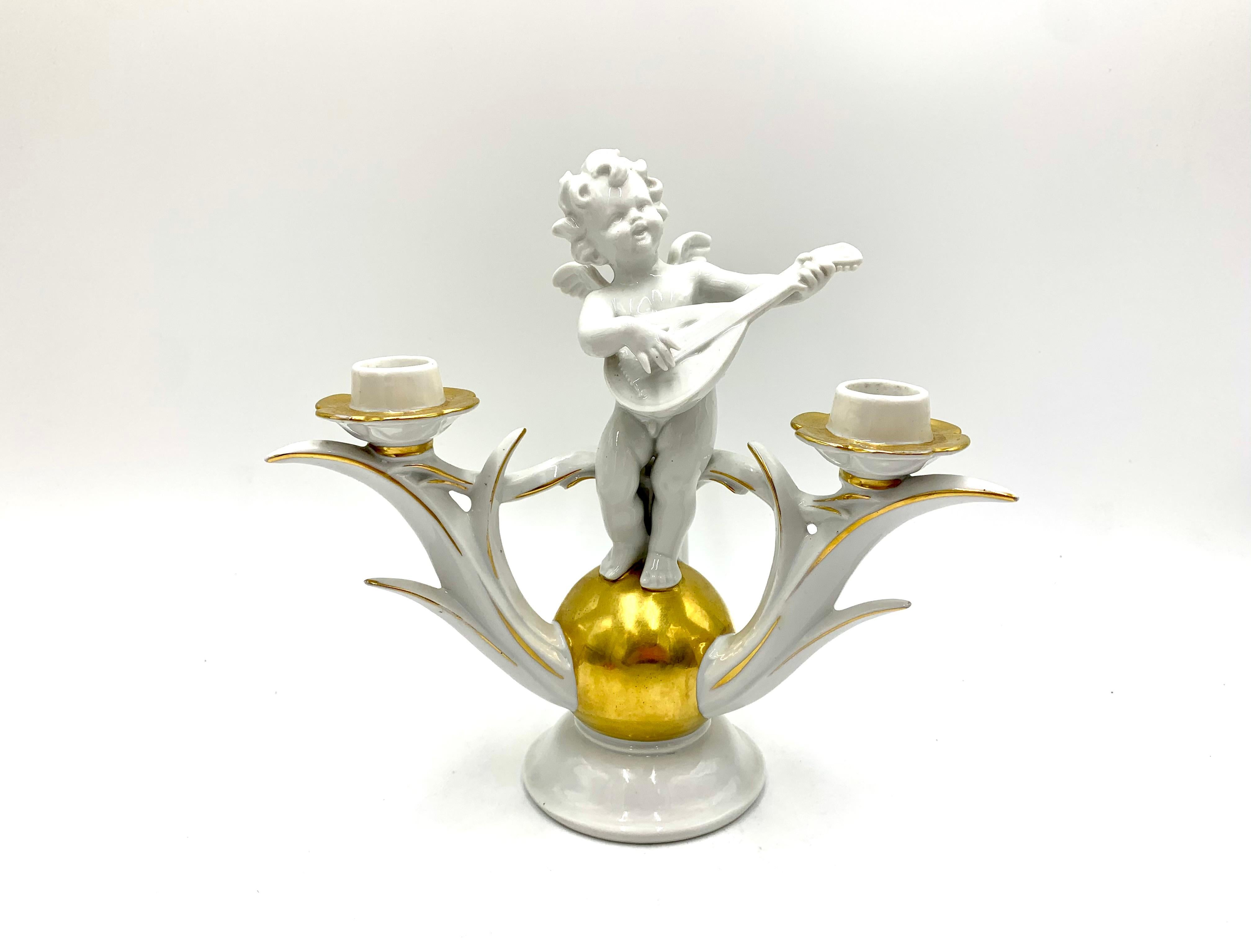A three-arm porcelain candlestick with gilding and a cupid motif with a mandolin on a golden ball. Signed with the orange Kunstporzellan signature. Manufactured in Germany by the renowned German manufacturer Carl Scheidig from Grafenthal, Thuringia,