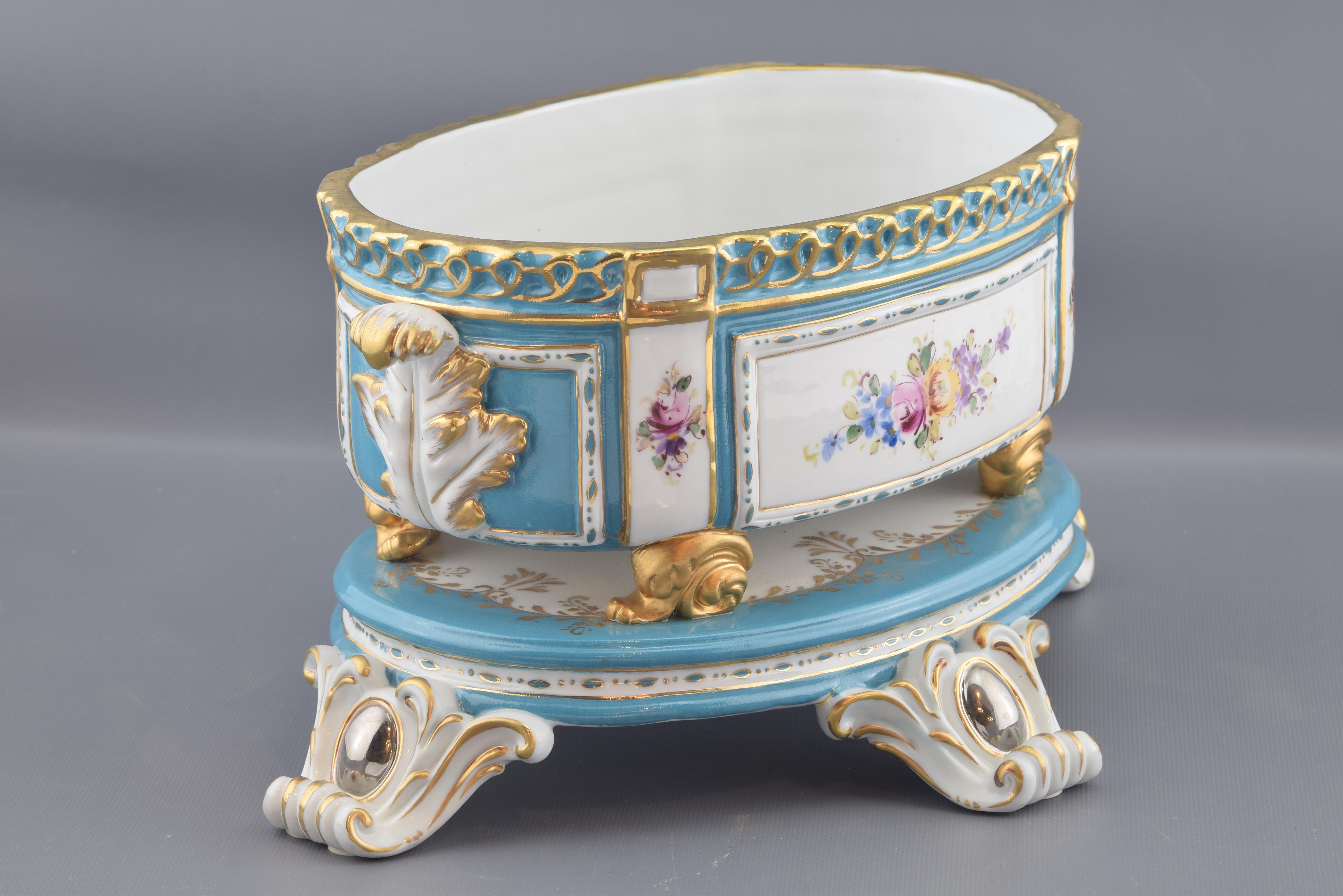 The oval base rests on four legs made with volutes, plant elements and oval mirrors. Above it, an oval box with two small handles is placed, decorated with rectangles with flowers, vegetal elements and an upper band in relief highlighted with golden