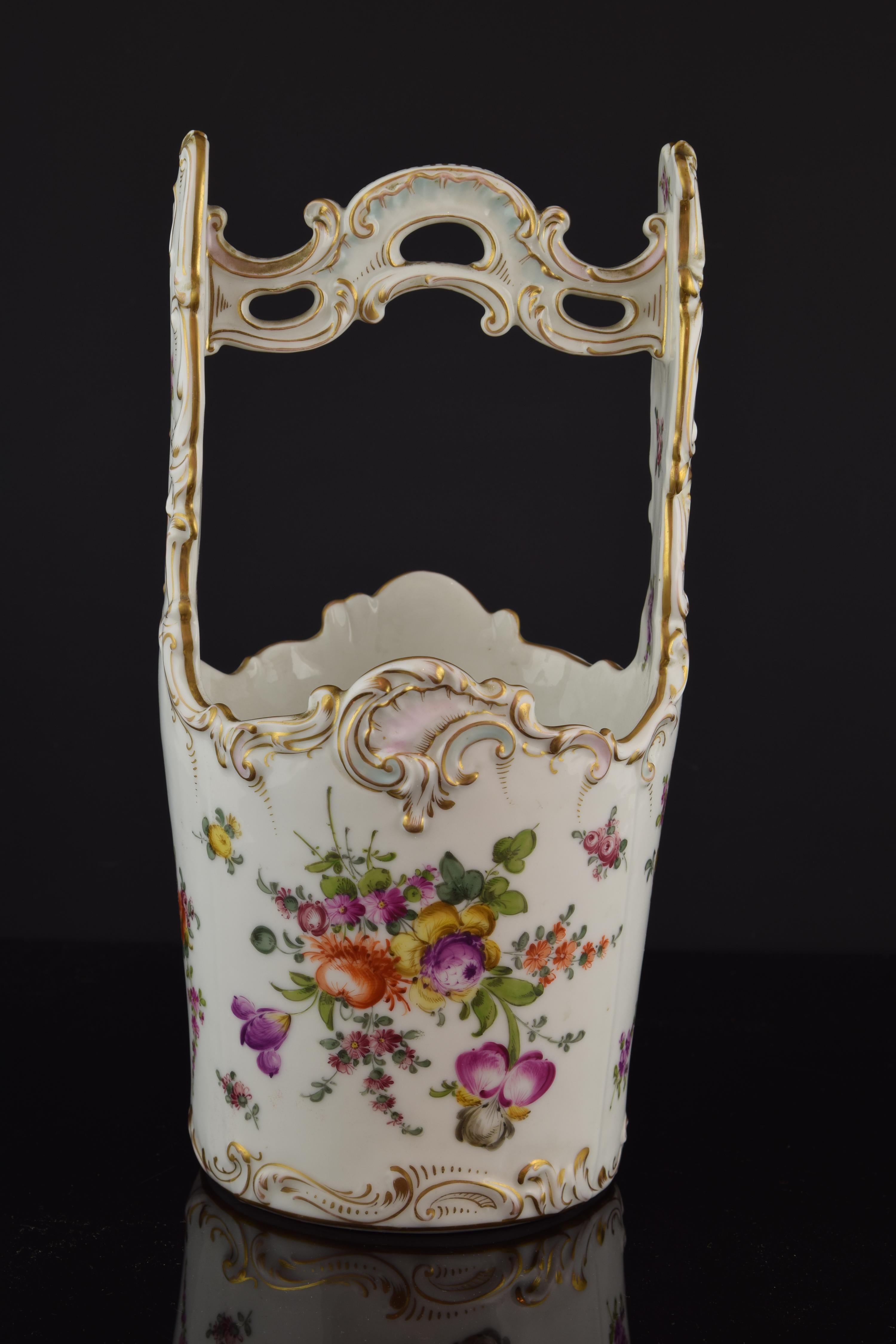 Pièce en porcelaine émaillée avec des détails dorés qui permet de placer des fleurs à l'intérieur. En forme de seau, elle possède une anse décorée de formes inspirées du rococo du XVIIIe siècle, qui sont également présentes sur le bord de la pièce