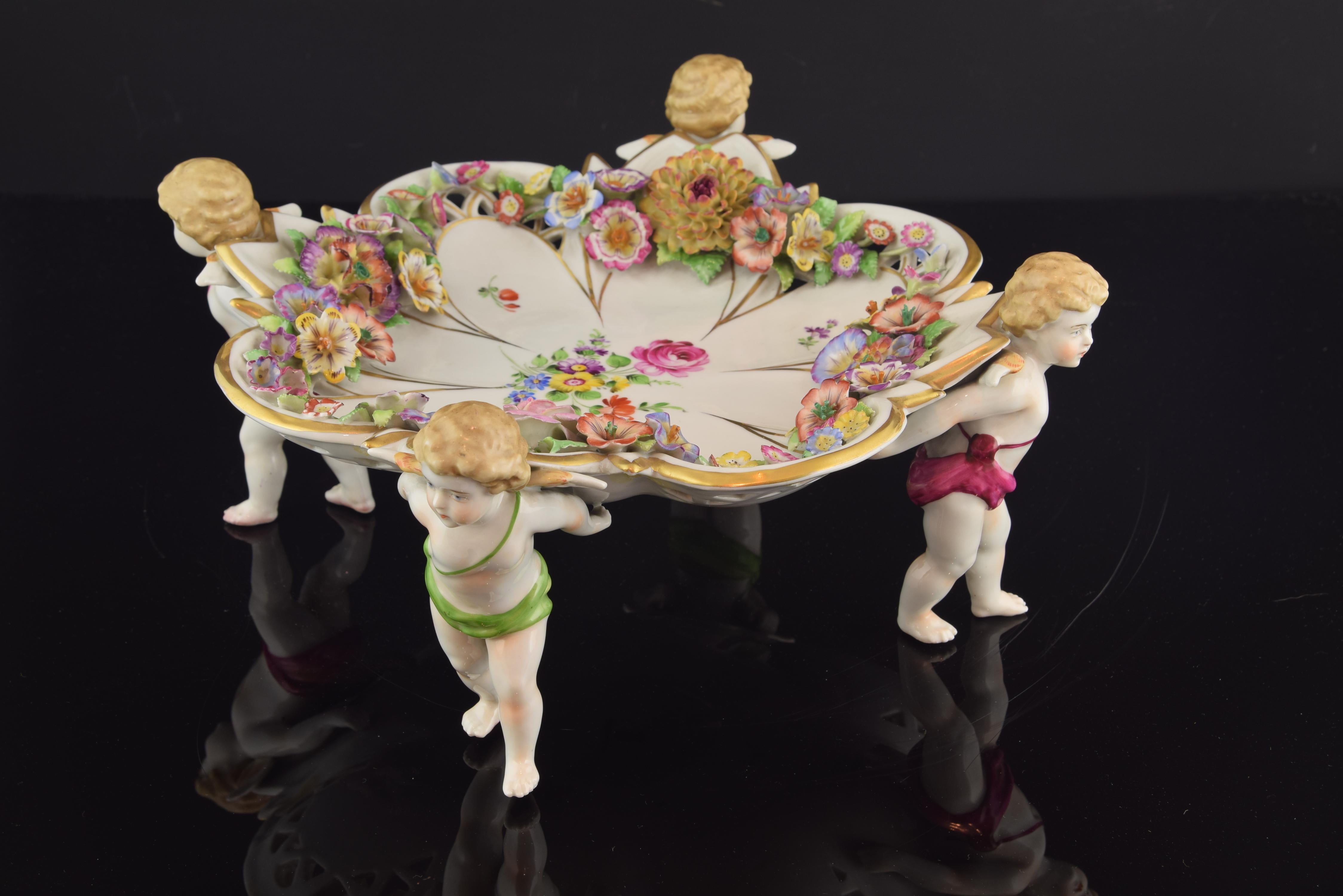 Centerpiece with four little angels or cupids holding on their backs a tray with a golden border and shaped like a flower and that has been enhanced with a multitude of delicate flowers in various shapes and colors. This area also has more flowers