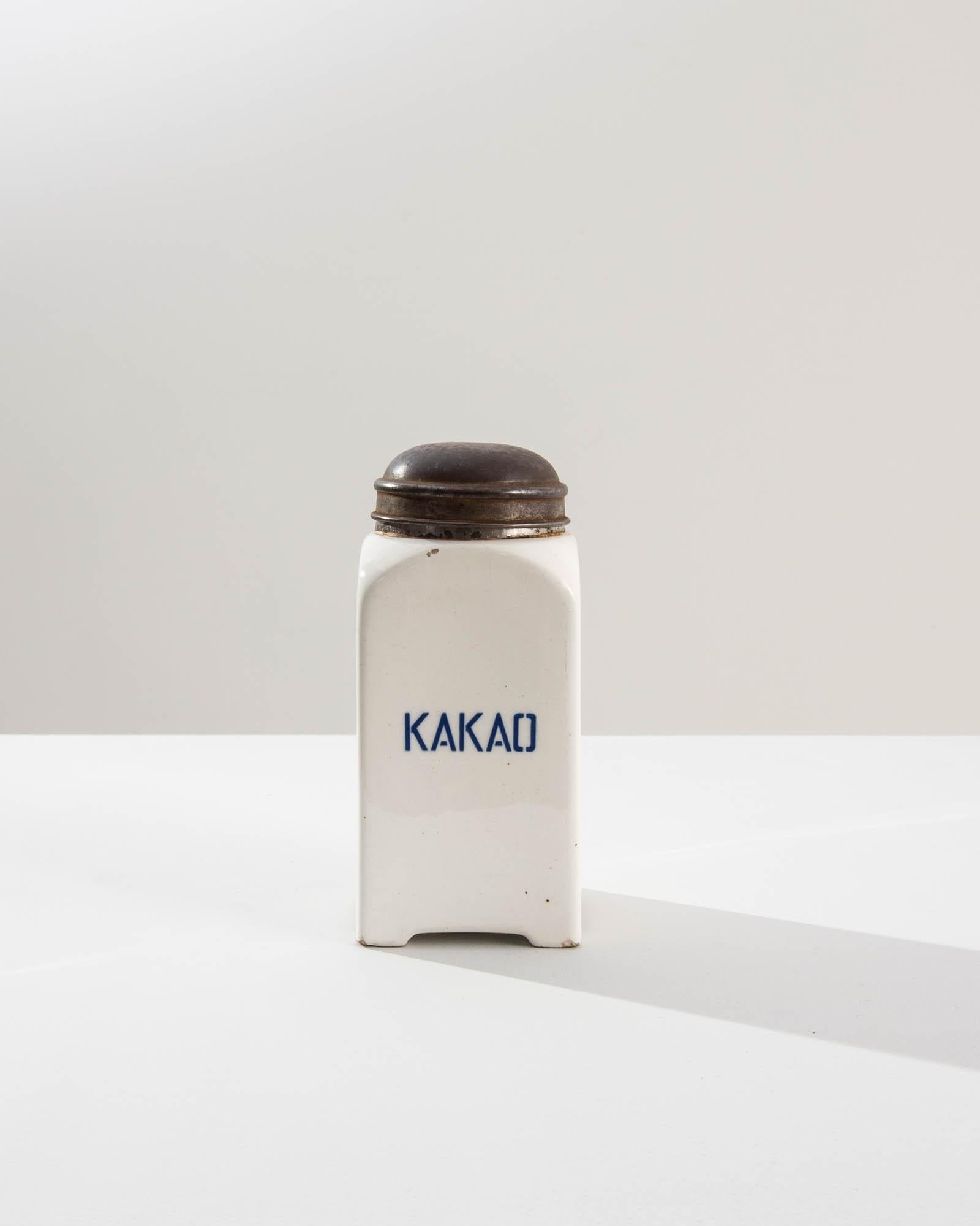 A vintage porcelain jar from 20th Century Germany, originally used for storing cacao. The slick white glaze is bright and inviting, attractive blue letters advertise the contents, ‘KAKAO.’ Subtly ornamented the metal lids feature raised ridges,
