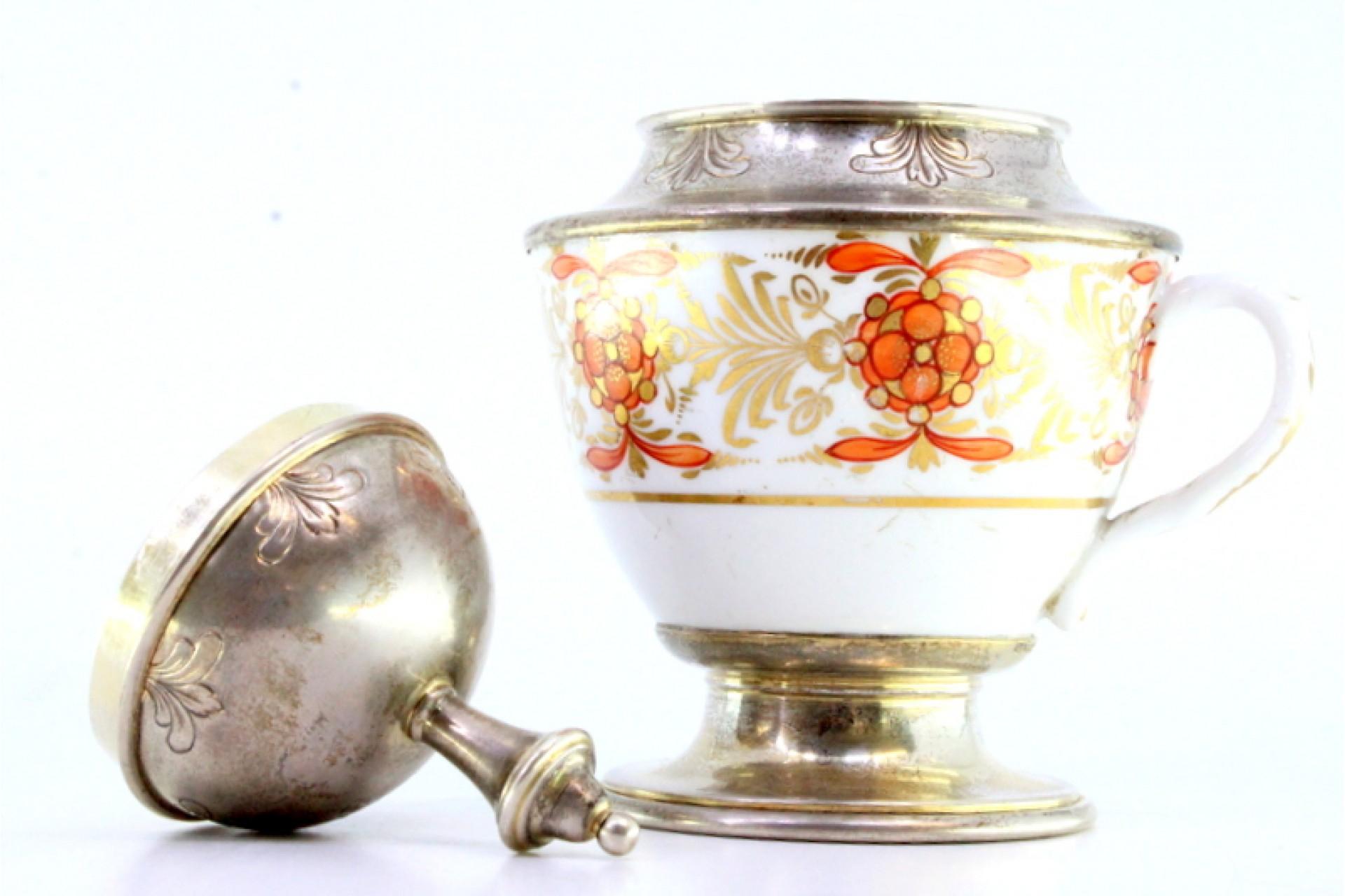 Description : Coupe en porcelaine avec anse en argent sur le couvercle et base circulaire avec frise environnante. Métal : Argent. Origine : Portugais. Marque : Cabeça de escravo. Poids : 185,94 grammes. Dimensions : 14cmx10cm. Contenu : 833/1000.