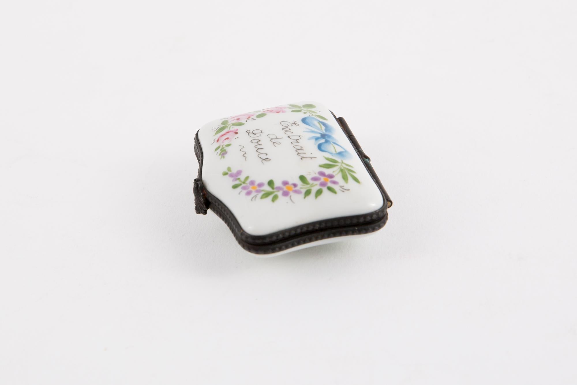 Porcelain Extrait de Douce (soft extract) polychrome pill box featuring a metal frame, a flower claps, leaves painted inside and a polychrome floral decor and text. 
Hand Painted
In good vintage condition. 
Width 1.5in. (4cm)
Length 2.3in. (6cm)
We