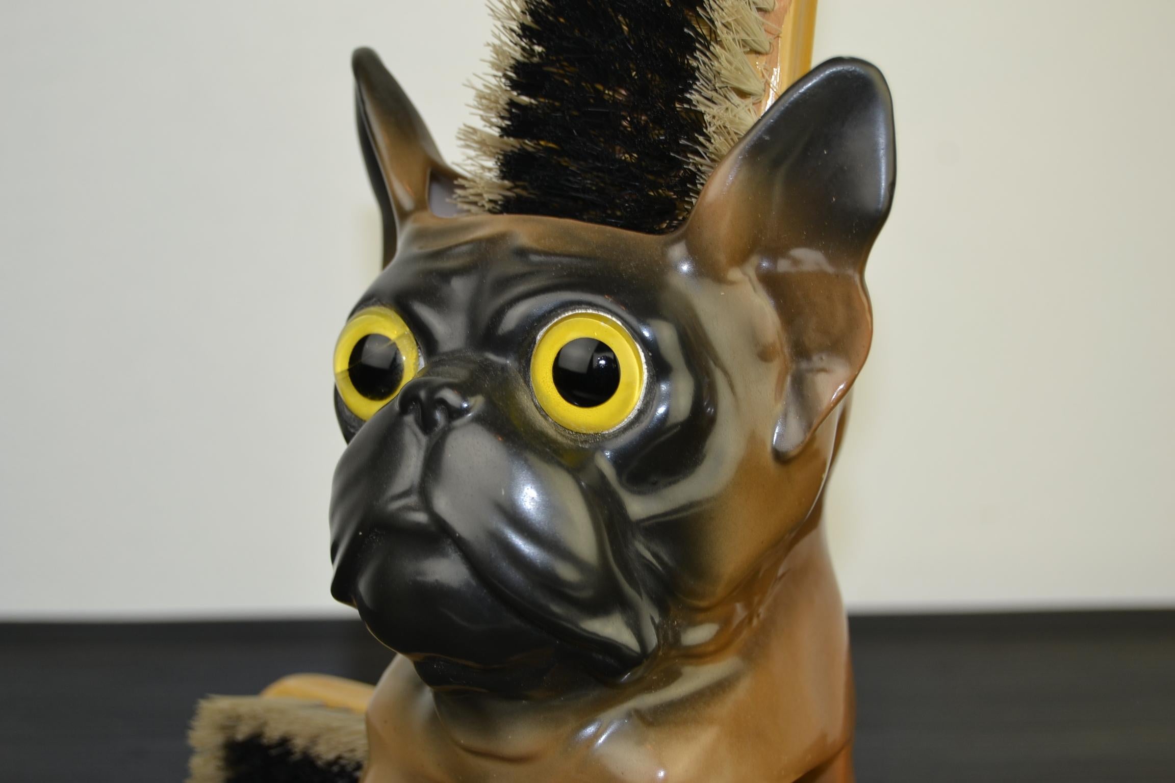 Porcelain French bulldog brush holder.
This European dog shaped brush holder is made of brown porcelain with a black snout, has two large glass eyes and space for two brushes. Dates 1930-1940.

The brushes have a floral motive. They have traces