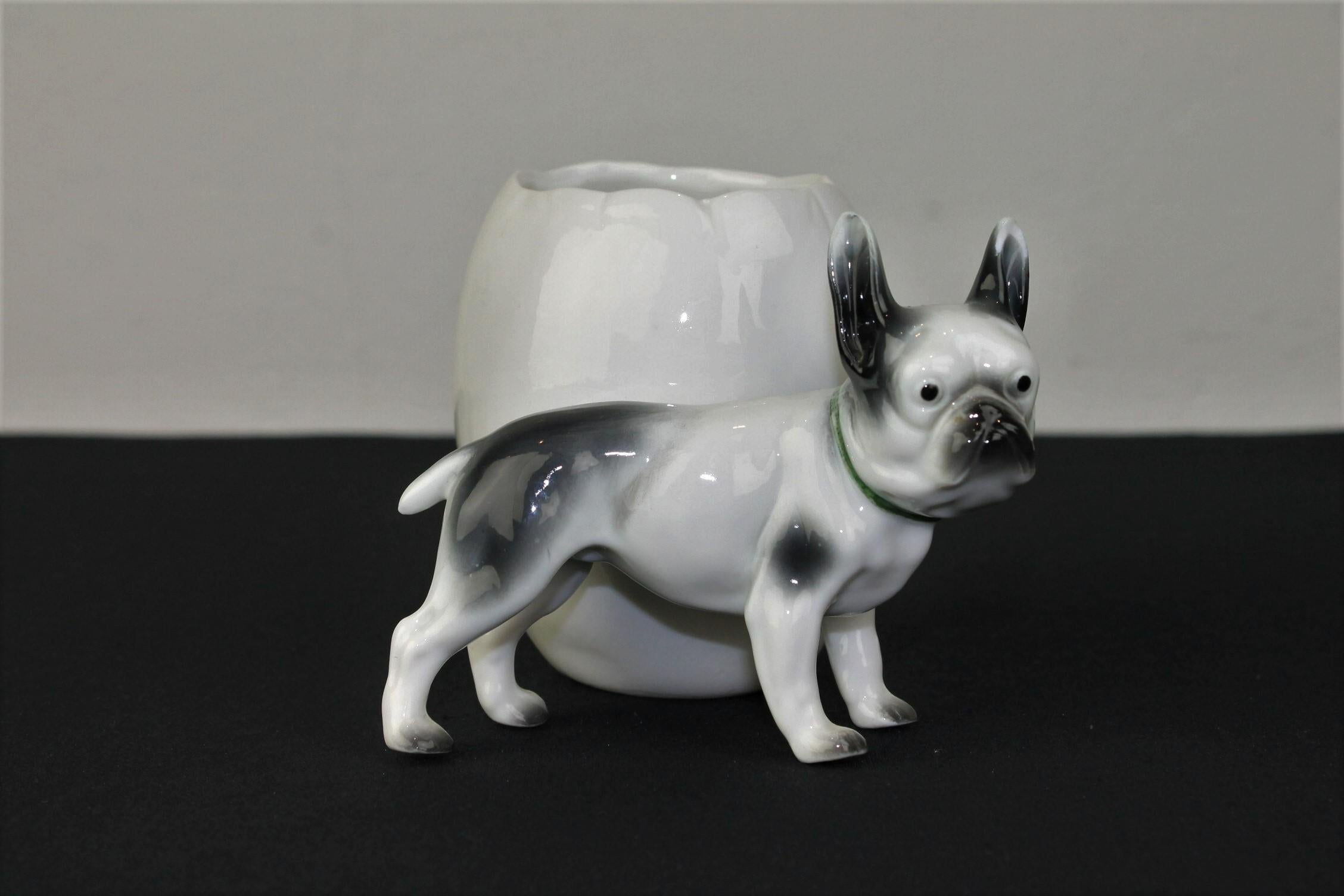 Porcelain French Bulldog sculpture with storage pot or planter.
It's a porcelain dog sculpture - dog figurine with an attached open storage pot which has a jagged edge like an egg. The white with grey Frenchie dog has a green collar around the