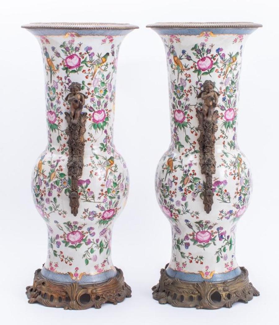 Late 19th century Gilded age style glazed porcelain flaring decorative vases mounted with gilt bronze base and cherub-form handles. Each vase features an hand painted with allover polychrome floral decoration and colorful exotic birds with gilt
