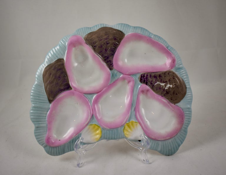 A late 19th century, French porcelain, crescent or half-moon shaped oyster plate, five pink blush oyster wells on a baby blue ground. Shown behind the main wells are the brown glazed backs of three oyster shells. Also shown are two smaller yellow
