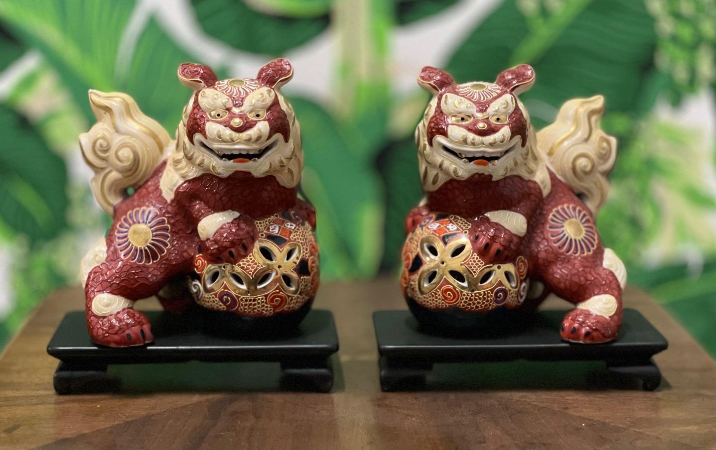 Pair of hand painted porcelain foo dogs from Japan feature a cinnabar body with colorful accents and gold detailing. Marked 