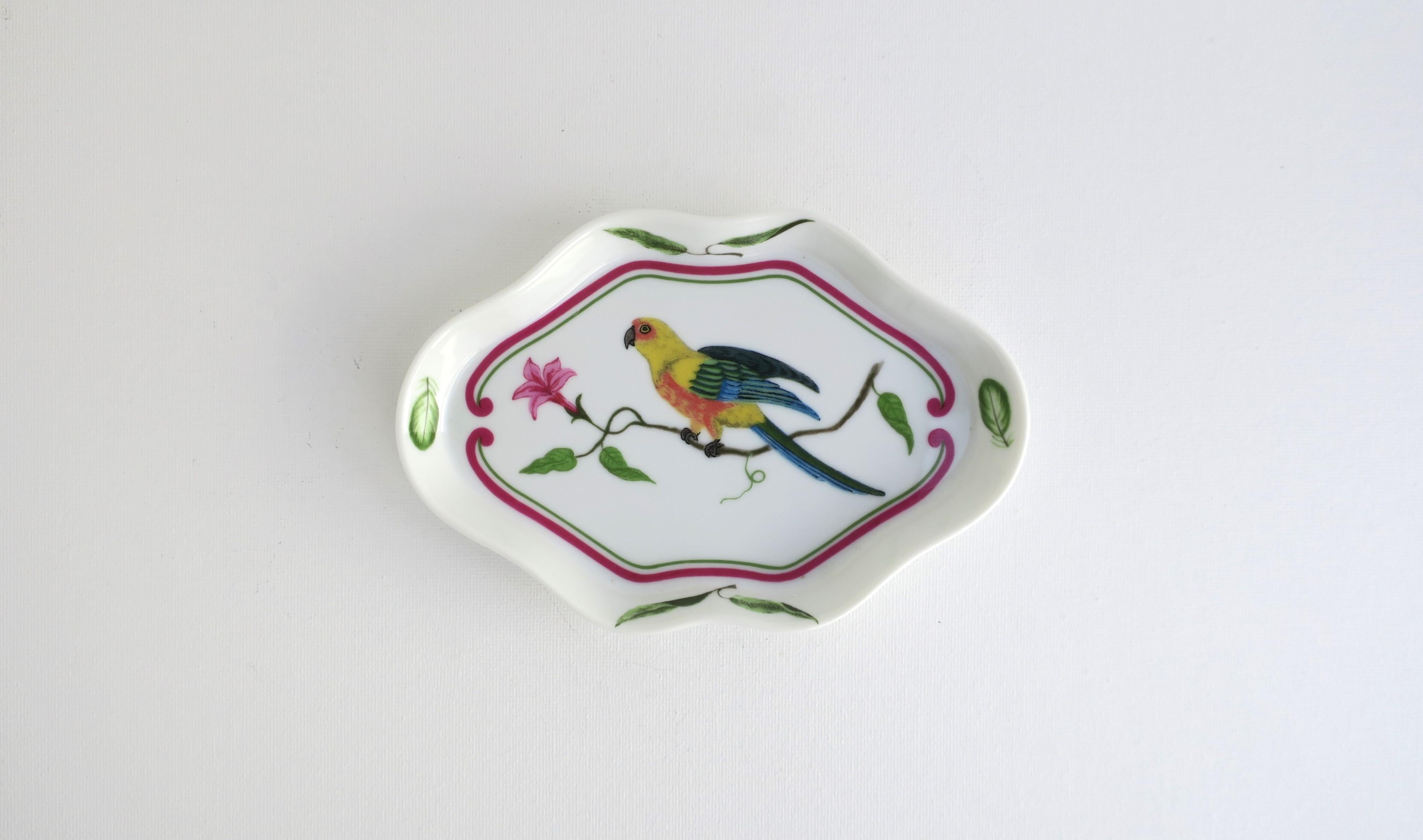 A very beautiful porcelain jewelry dish with tropical parrot bird design, circa 1980s, USA. Piece was made in 1989 as marked. Dish is oblong with scalloped edge, beautiful parrot bird front and center sitting on a hibiscus flower branch, outlined in
