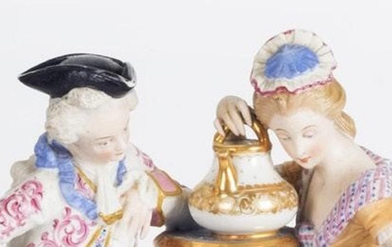 Bisque porcelain, hand painted, gilded. French, late 19th century.

A 19th century porcelain mantle clock with porcelain figures of a couple holding a teapot. The round shaped clock is surrounded by a stylized bow and gilded garlands and rests on a