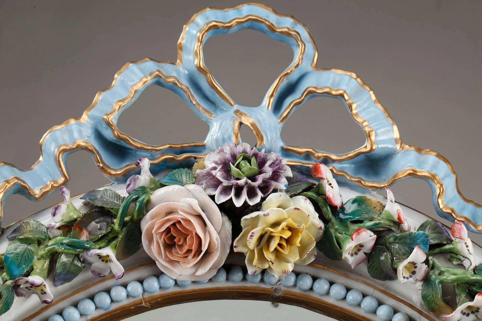 French mirror crafted of porcelain in Meissen taste. Exquisitely painted in polychrome with gilt accents, the bountiful frame is adorned with Rococo decoration, composed of a wide variety of highly detailed flowers and a frieze of pearls. It is