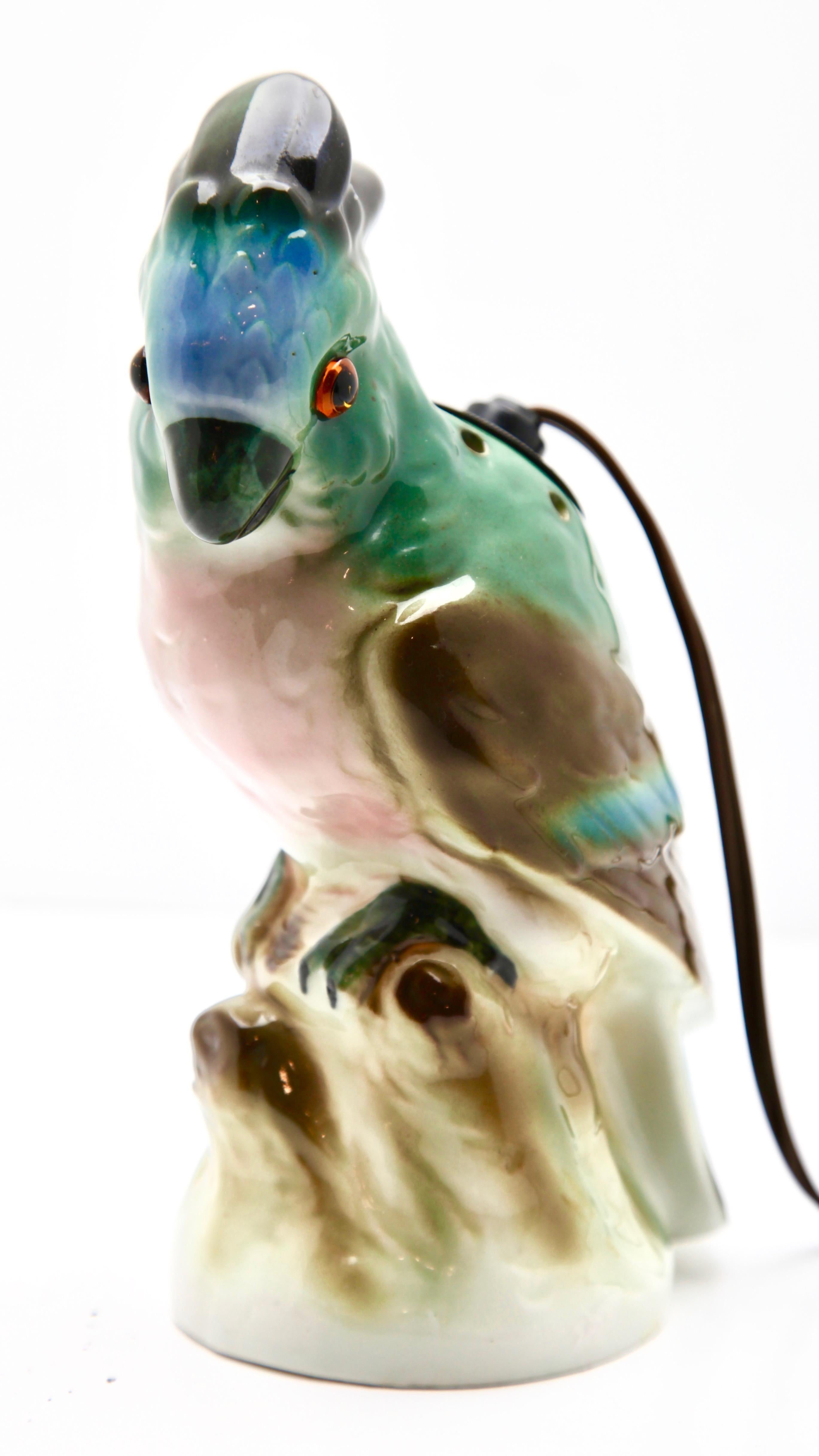 Made in Germany during the 1930s, this porcelain figurine is also a room aromiser and nightlight or table lamp.
Modelled as a cockatoo perched on a rock with hand painted plumage in blues, browns and greens. This friendly bedside companion features