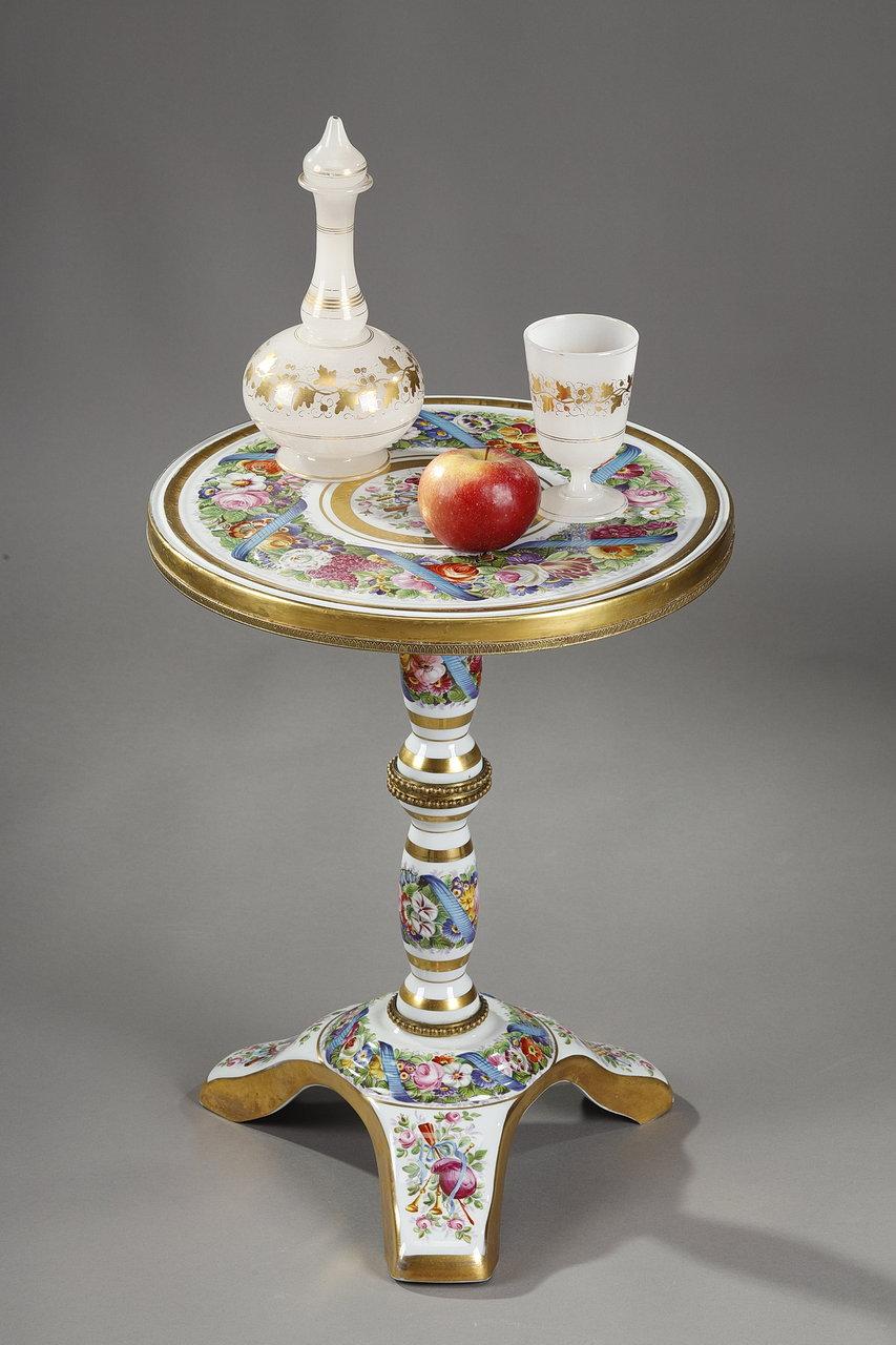 Table guéridon in white enamelled porcelain, resting on a tripod foot, from the Napoleon III period. This small pedestal table is enamelled with a rich decoration of polychrome flowers in crown on the tray, the baluster shaft and the base. The
