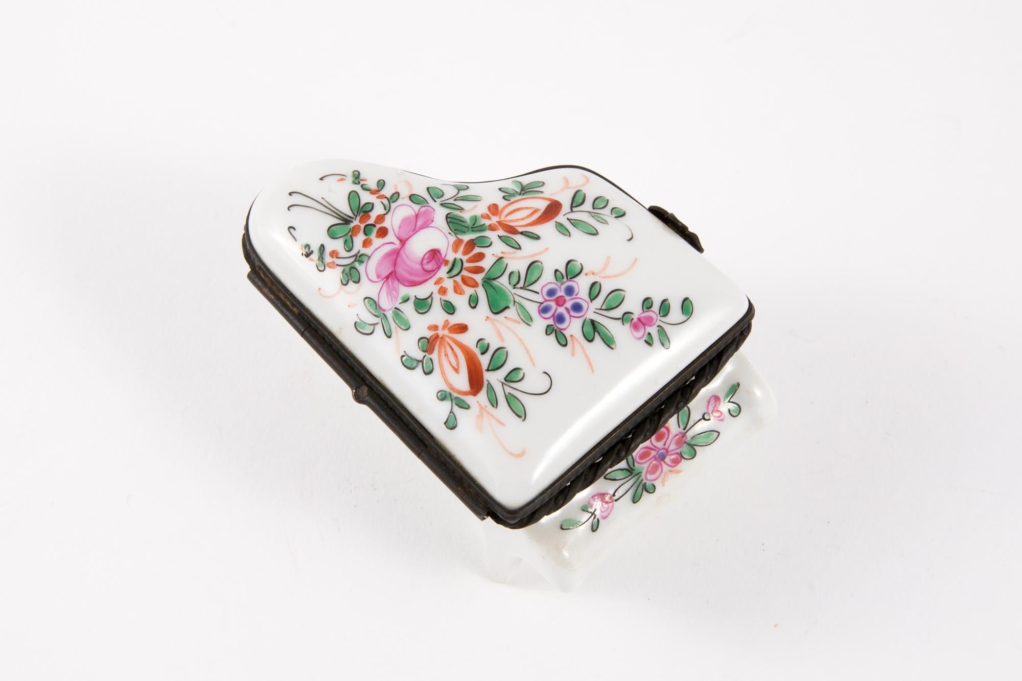 Porcelain piano shaped pill box featuring a flowers stage decor, a metallic black tone hook to keep it open.
In good vintage condition. Made in France. 
Height Closed 1.7in. (4,5cm)
Maxi Width 2in. (5.5cm)
Maxi Length 2.7in (7cm)
We guarantee you