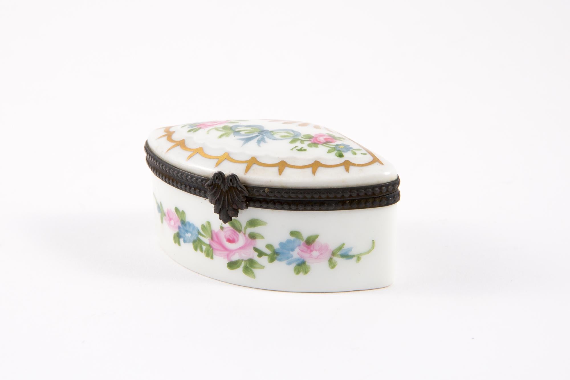 Porcelain pill or medicine box featuring a triangle shape, a black metal frame decorated with multicolour flowers painted on top, a tarnish tie claps opening. 
In good vintage condition. Made in France. 
Length 2.7in (7cm)
Height 1.7in. (4,5cm) 