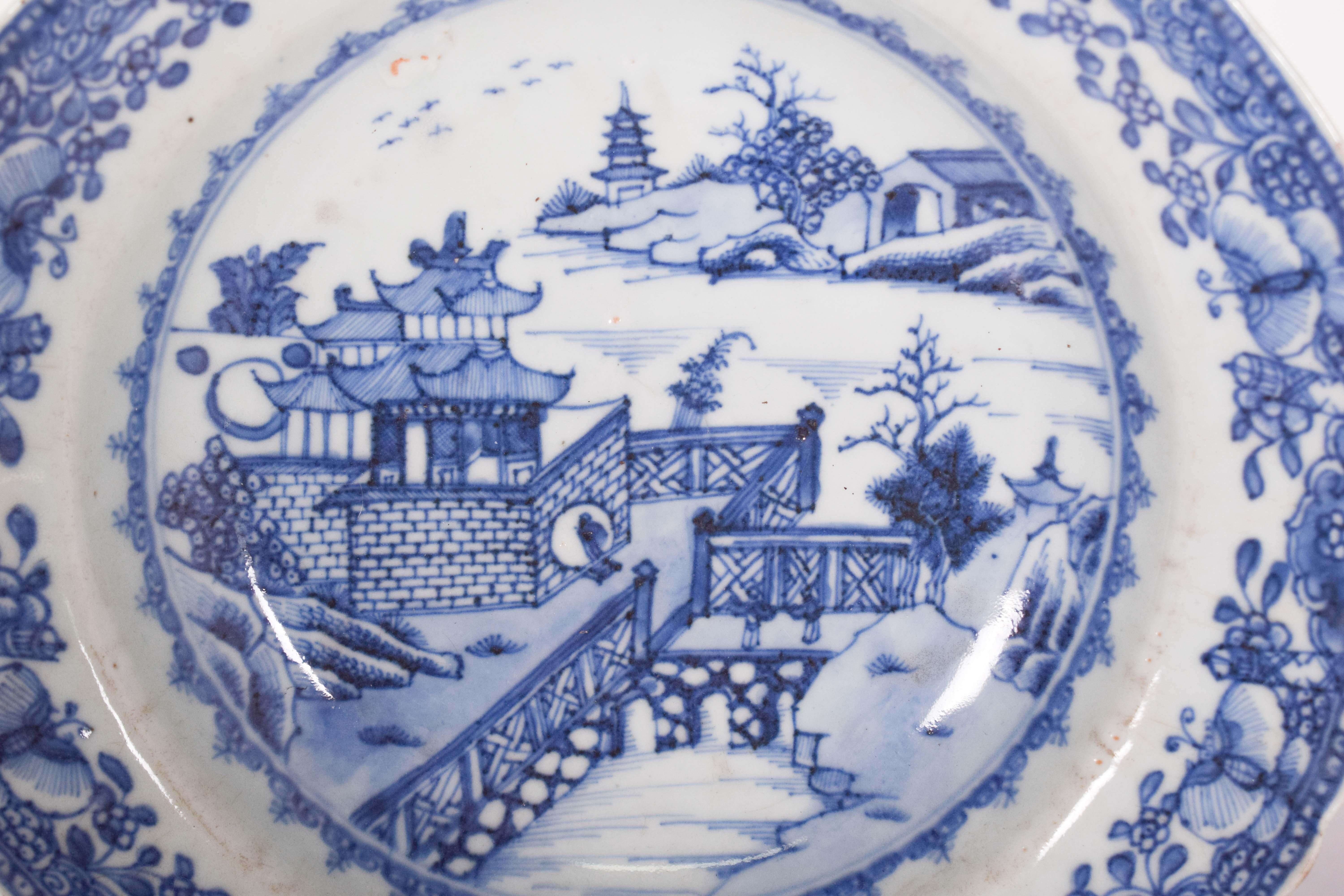 Porcelain plate from China for export. Blue and white decoration, depicting a river landscape with pagodas and a bridge, with flowers and butterflies on the edges, Qing dynasty, Qianlong period (1736-1795).
In the center, a Chinese pagoda rises