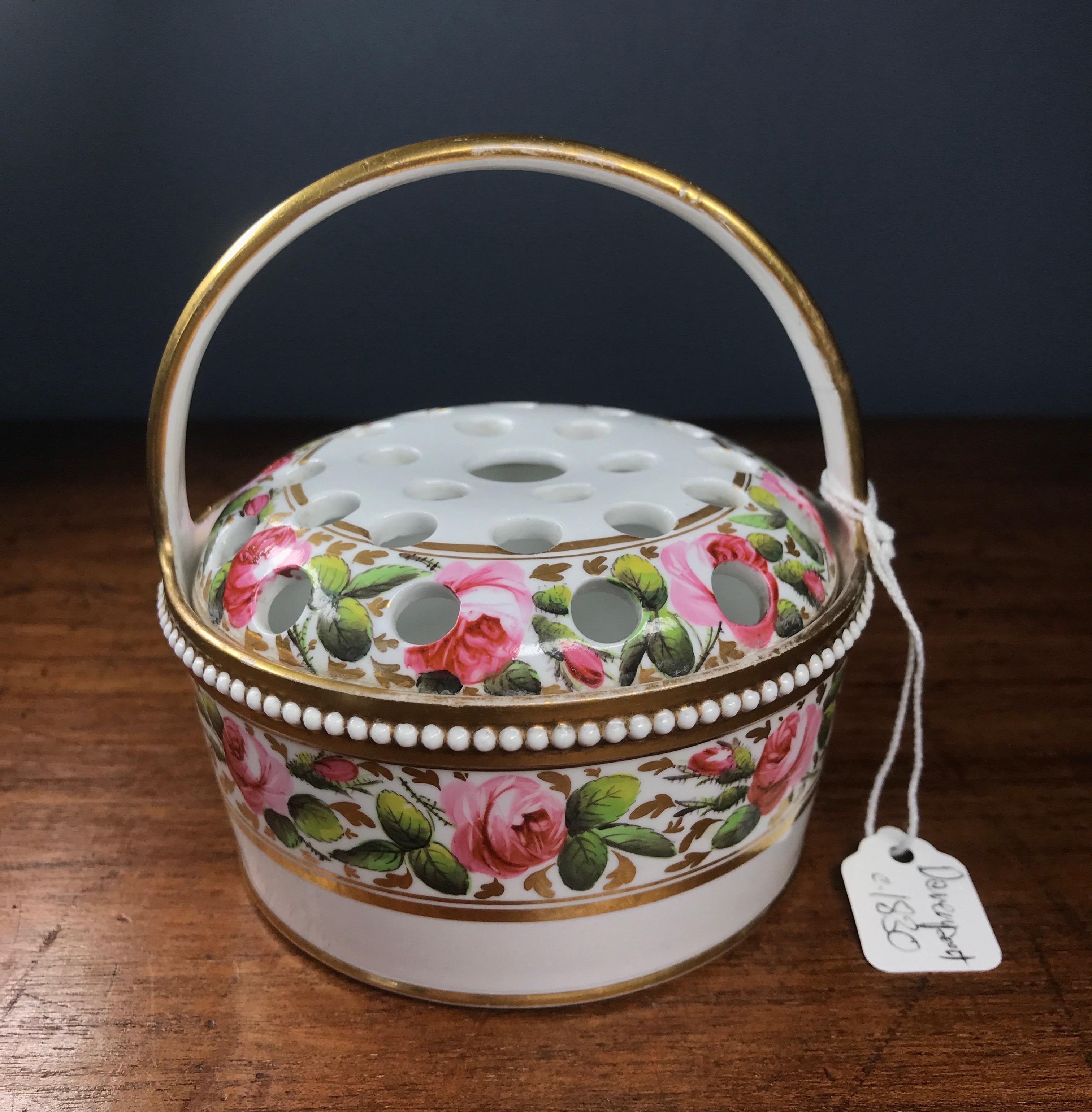 English bone china potpurri basket and pierced cover, decorated with wide bands of roseheads and gilt foliage, the rim with a beaded moulding, a high handle overhead.

Pattern no 1533 in gold, possibly Davenport. Circa 1830.