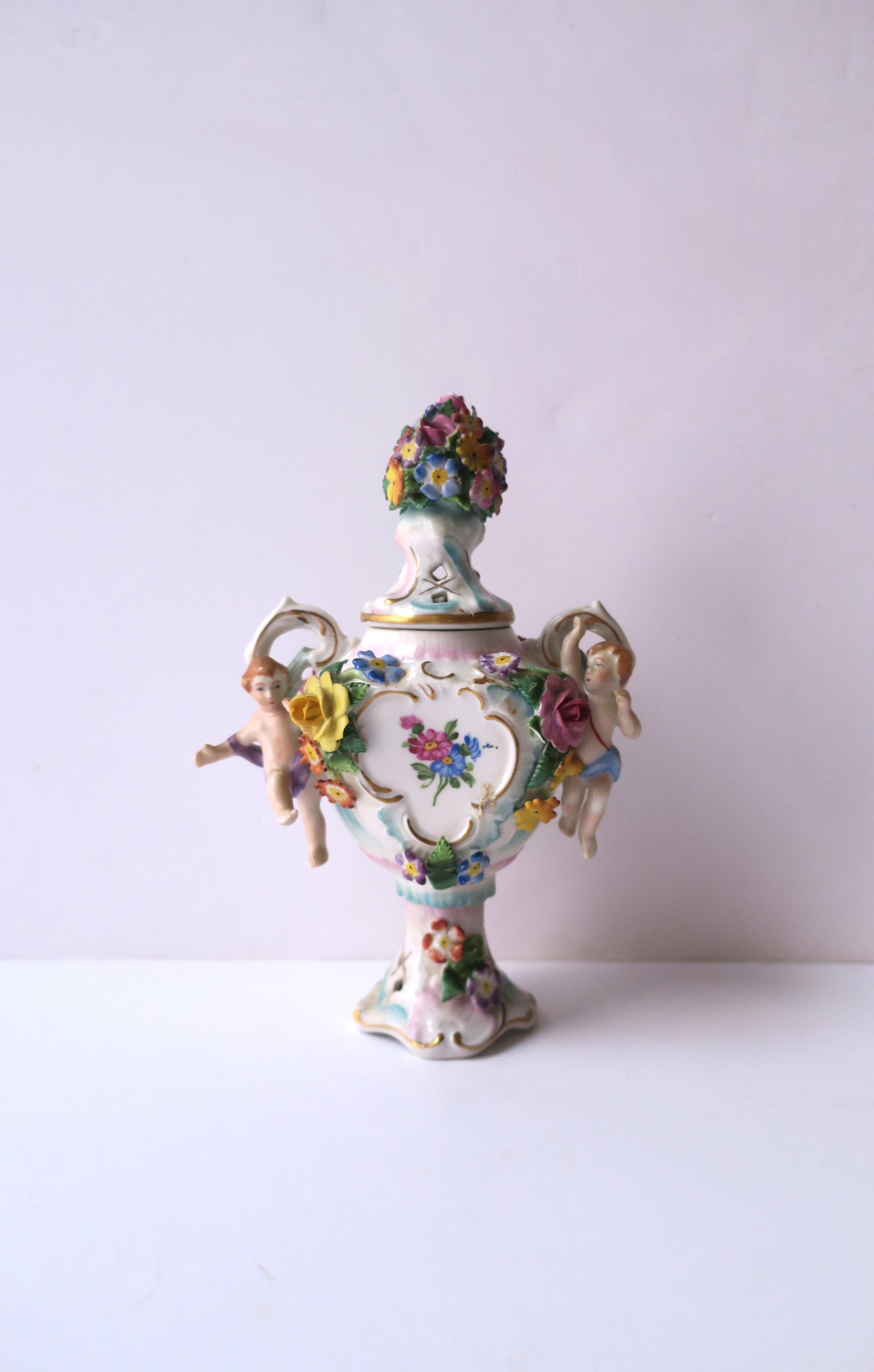 A beautiful German hand painted porcelain potpourri urn vase with flowers and putti, in the Rocco style, by Sitzendorf, circa 19th century or earlier, Germany. Piece has details floral lid, putti and flowers on front left and right sides, flowers on