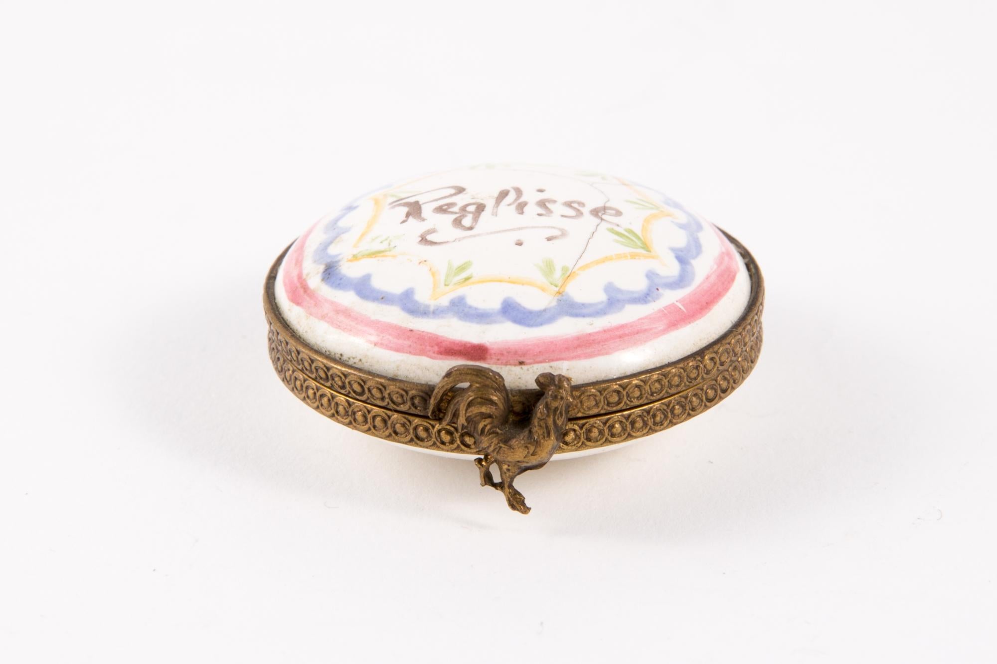 Porcelain Reglisse: Licorice (soft extract) polychrome round pill box featuring a metal frame, a flower claps, leaves painted inside and a polychrome floral decor and text. 
Hand Painted
In good vintage condition. 
Diameter 1.5in. (4cm)
Width 0.6in