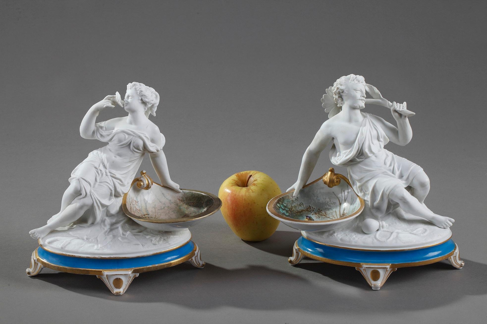 Pair of antique ring holders crafted in bisque? porcelain? featuring a man and a woman posed in classically-inspired robes. They are lying on a rock near a small dish with polychromatic decoration of birds in a landscape. The bisque figurines are