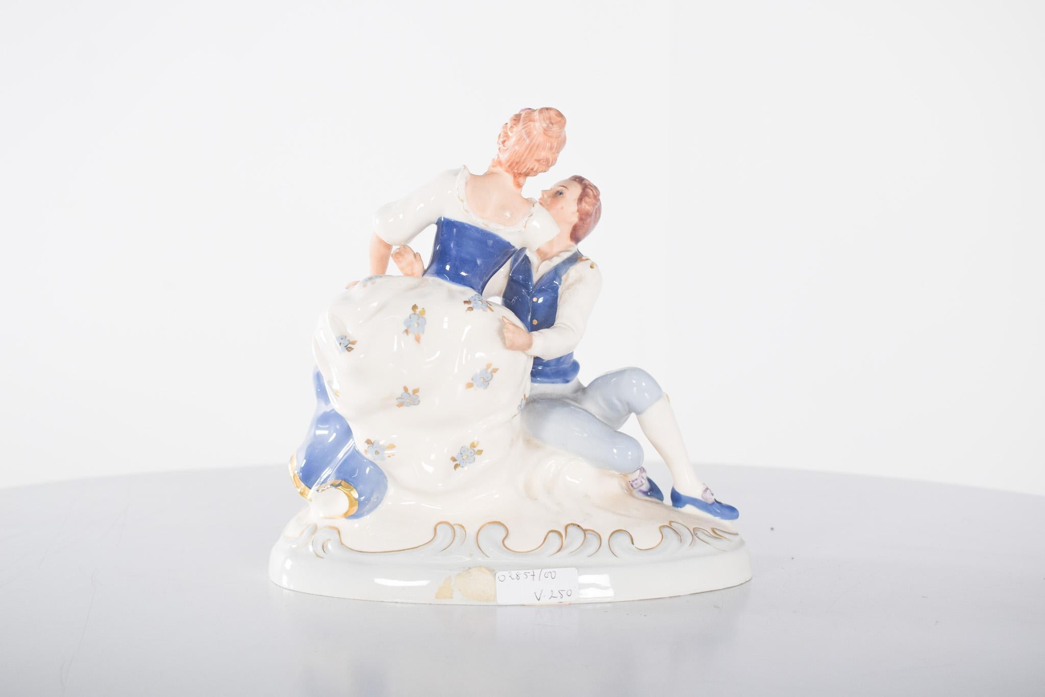 Scultura in porcellana di una signora e un gentiluomo seduti.  Raffigura una scena romantica tra un gentiluomo e una signora seduti, evocando lo stile elegante del XVIII secolo. L'opera raffigura un giovane galante seduto ai piedi della signora, che