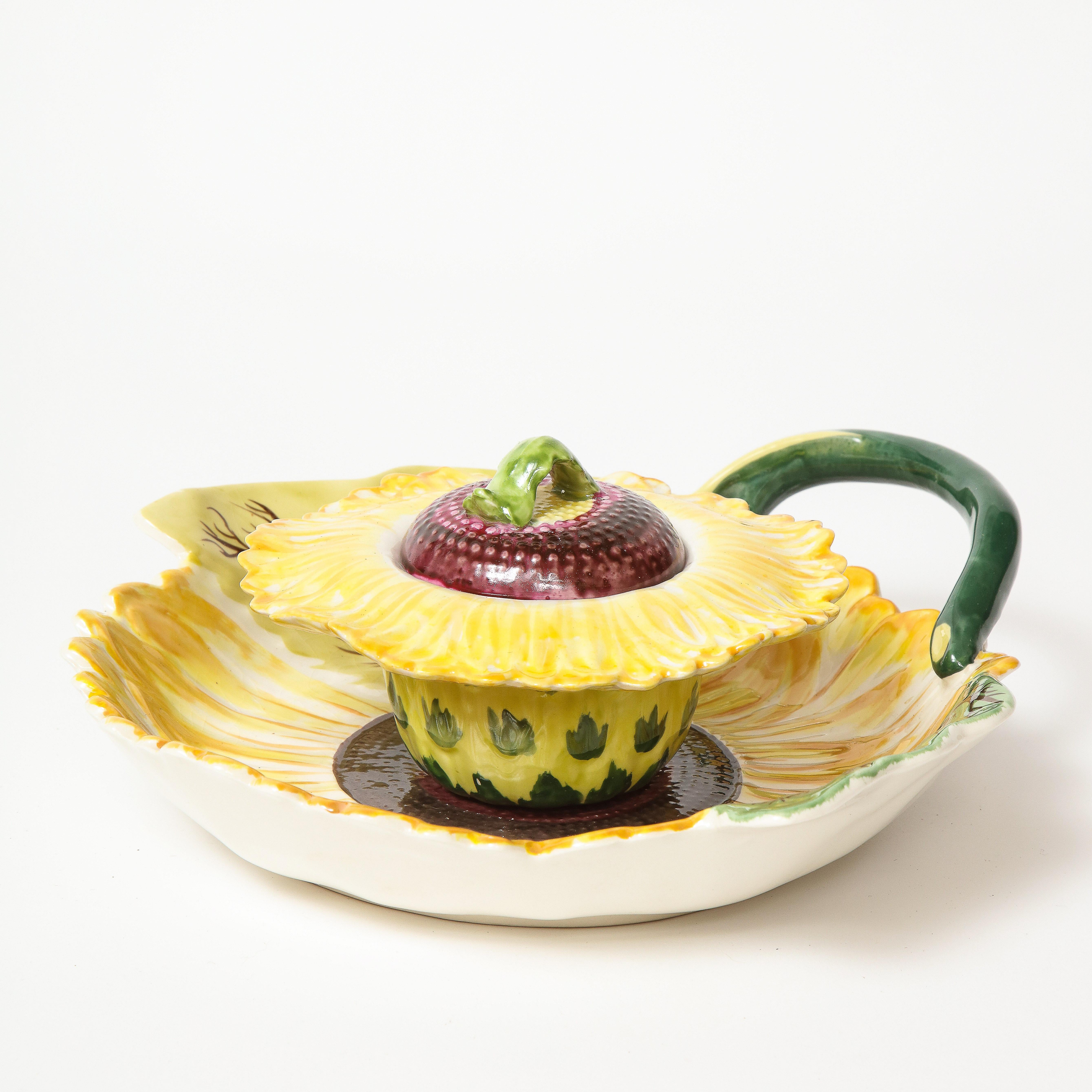 Comprising a central, removable disk flower in two parts, the underdish also depicting sunflower petals, with a green stem-form handle and green leaves. Makers mark on bottom, Mottahedeh, England.