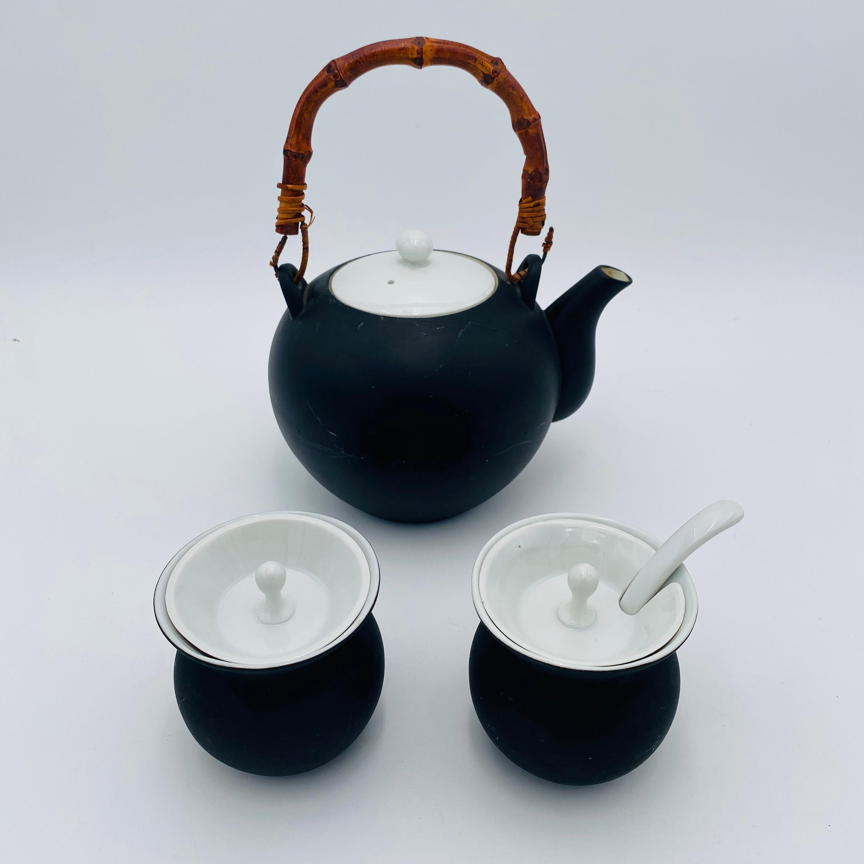 Raro juego de tetera de porcelana con crema y azúcar  diseñado por Lagardo Tackett para Freeman Lederman. El juego de tetera tiene un bonito exterior negro mate y un interior de porcelana blanca. La tetera tiene un asa de caña. Todas las piezas
