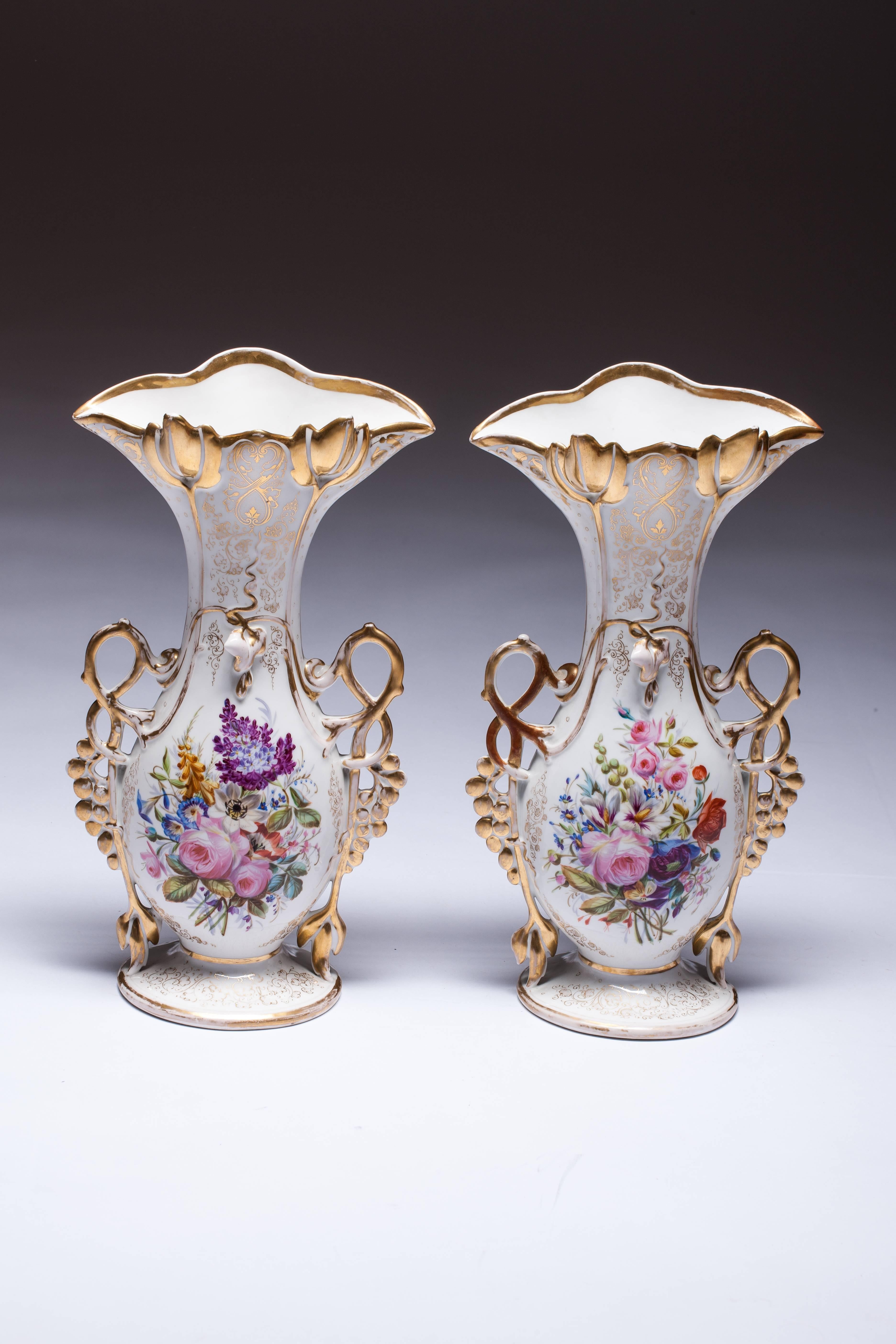 This is a highly ornamental pair of Old Paris porcelain mantel vases decorated with heavy gold, applied morning glory flowers, and hand-painted scenes of flower bouquets. 

These are a perfect example of Rococo ornamental wares made in the