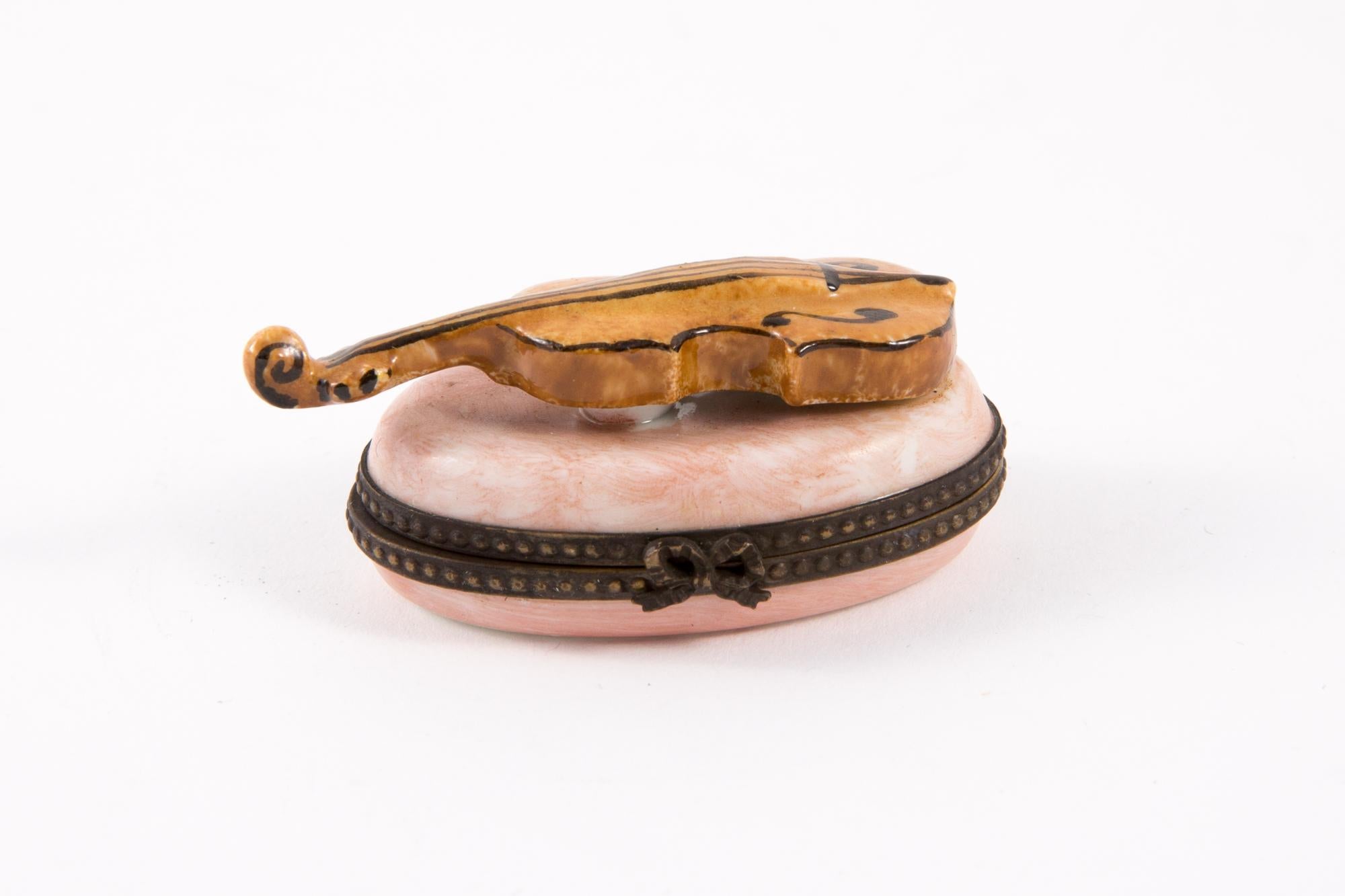 Limoges Porcelain violin pill or jewel box featuring a metal frame, a bow claps, leaves painted inside and a top violin on the pink box.
Hand Painted
In good vintage condition. 
Width: 1.7in. (4.5cm)
Length: 2.3in. (6cm)
Heigth: 1.18in. (3cm) 
We