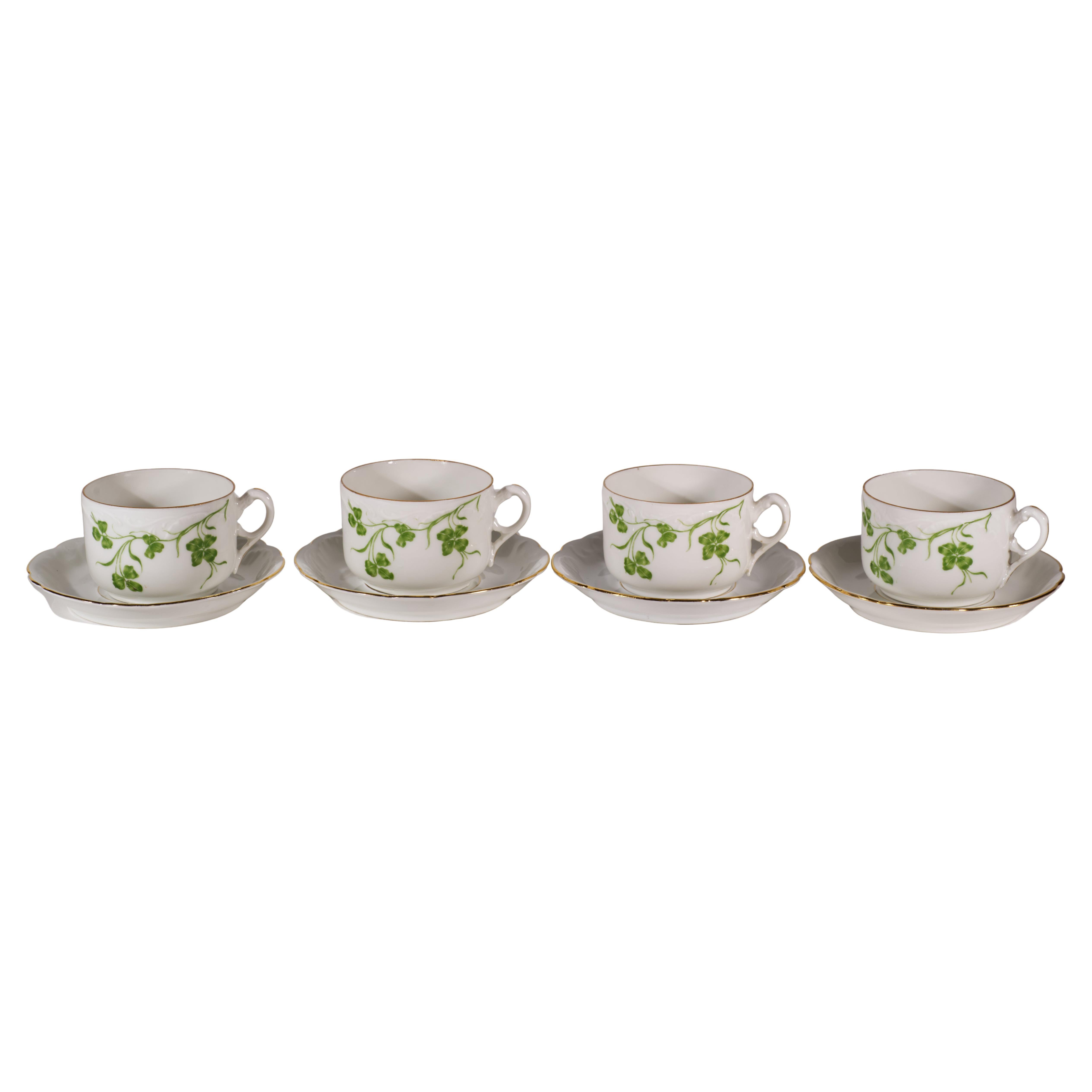 El juego de tazas y platillos de porcelana antigua presenta delicados motivos monocromáticos de hojas y tallos de trébol verde con adornos dorados en los bordes y decoración dorada en las asas ornamentadas. Las piezas en bruto de porcelana china