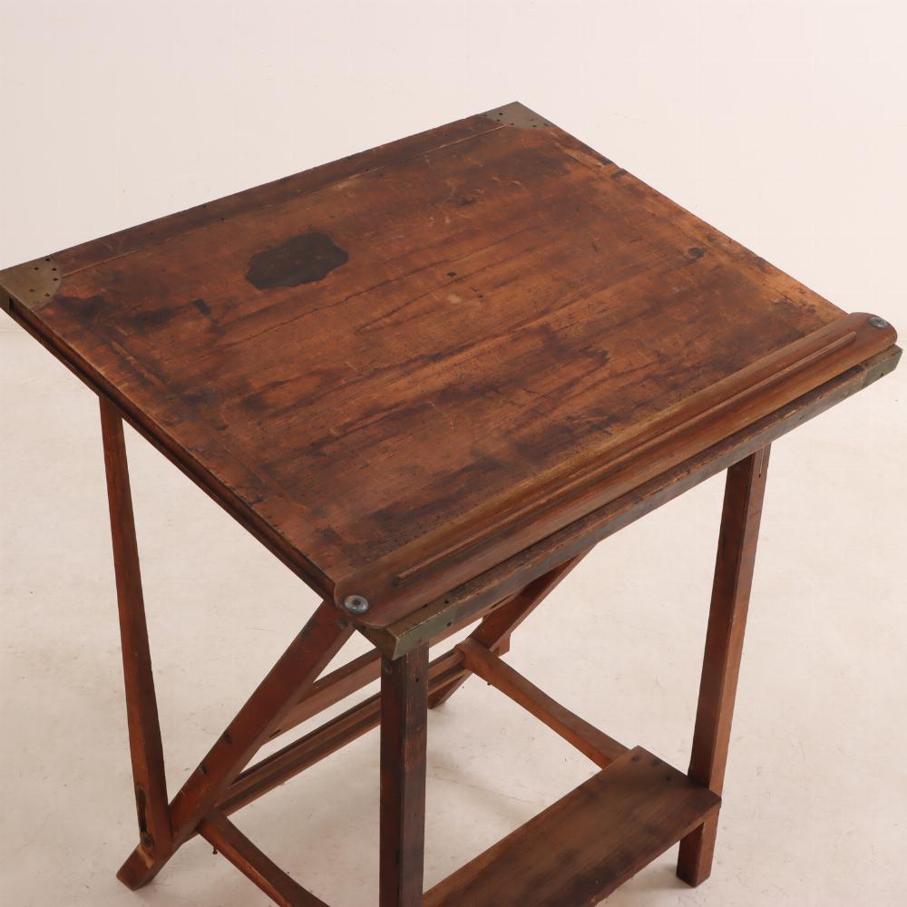 This early 20th century wooden folding draftsman's table has its original slide tool and brass fittings.  

This table has a nicely aged patina. It's sturdy and in overall excellent condition besides the obvious age-appropriate wear. 

Drafting