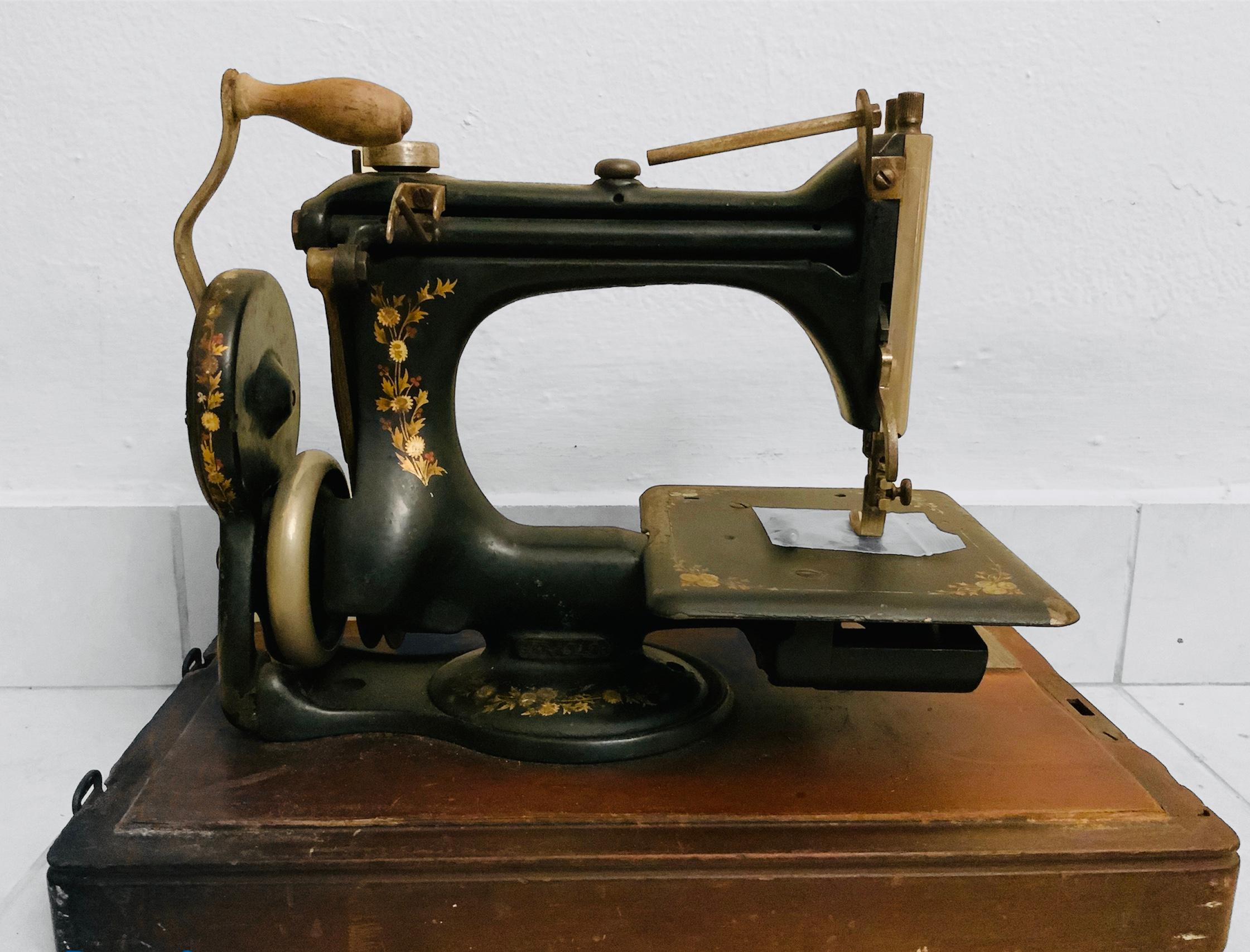 This is a portable Singer Manufacturing Co. domestic manual sewing machine model 24-61. It is metal painted black and adorned with decals of cornflowers and red berries. It is mounted in a wood rectangular base and covered with a dome shaped lid