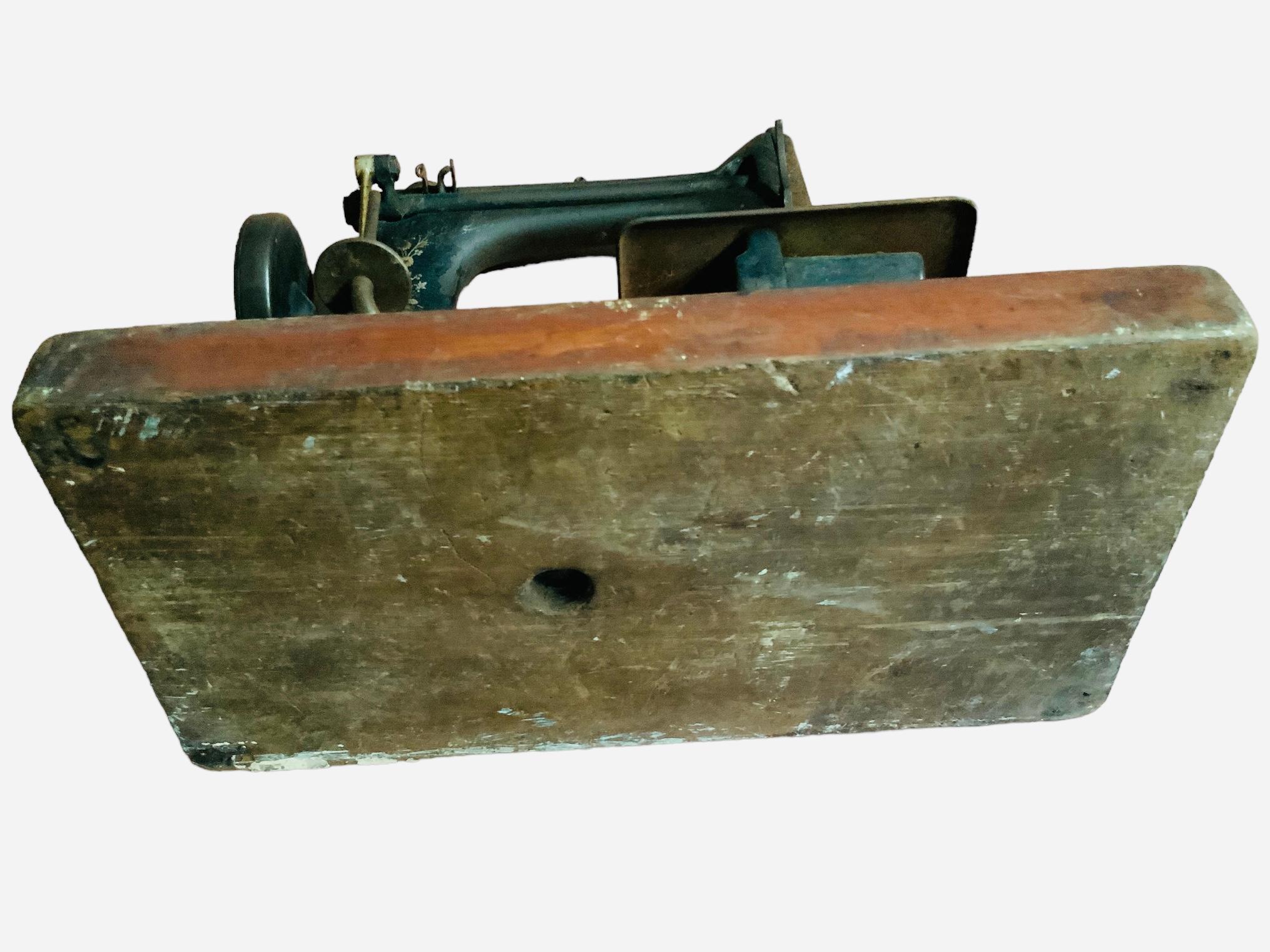 This is a portable Singer Manufacturing Co. domestic manual sewing machine model 24-61. It is made of metal painted black and adorned with decals of cornflowers and red berries. It is mounted in a wood rectangular base. The Singer gold tone metal