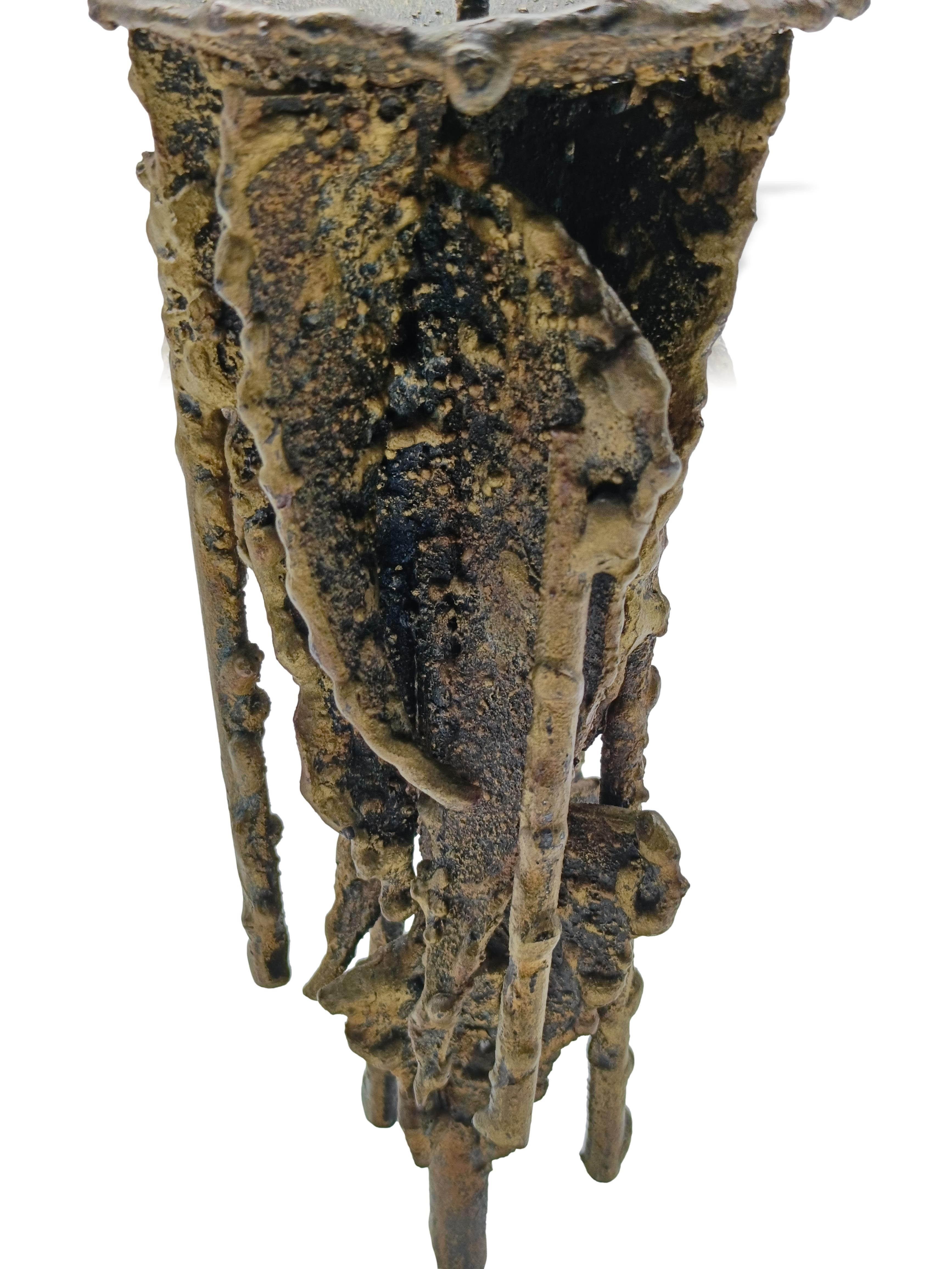 Questo eccezionale candeliere è un vero e proprio pezzo d'arte scultorea, non un semplice oggetto funzionale. Realizzato in metallo fuso, presenta una superficie grezza  che simula la cera che cola o una fusione organica e spontanea. Firma incisa