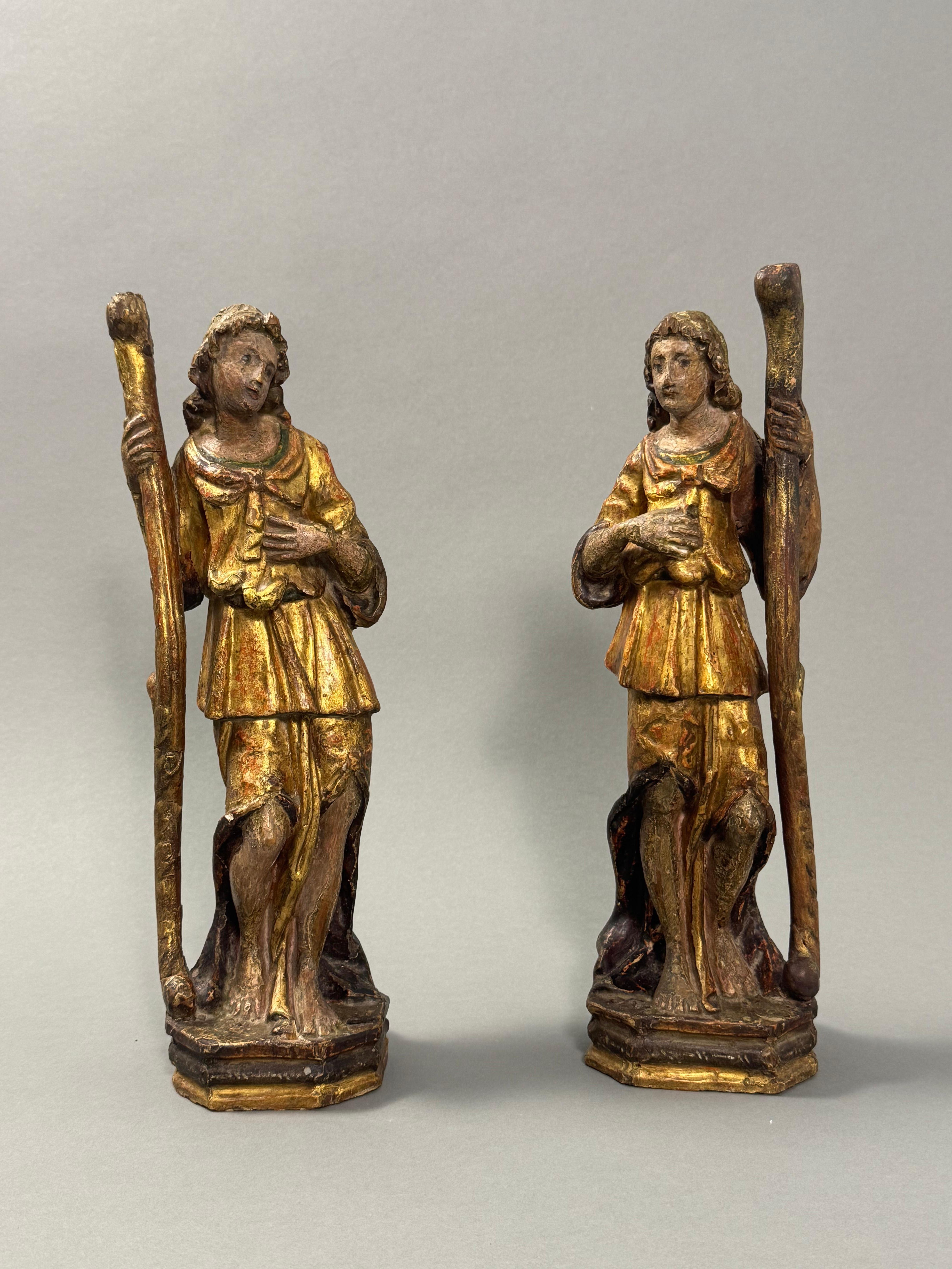 Portacandele in legno dorato con tracce di policromia della fine del XVII secolo, raffiguranti due figure religiose con bastone tipiche dell'arte sacra. Le espressioni sono composte e l'abbigliamento è tipico delle statue votive o decorative. Data
