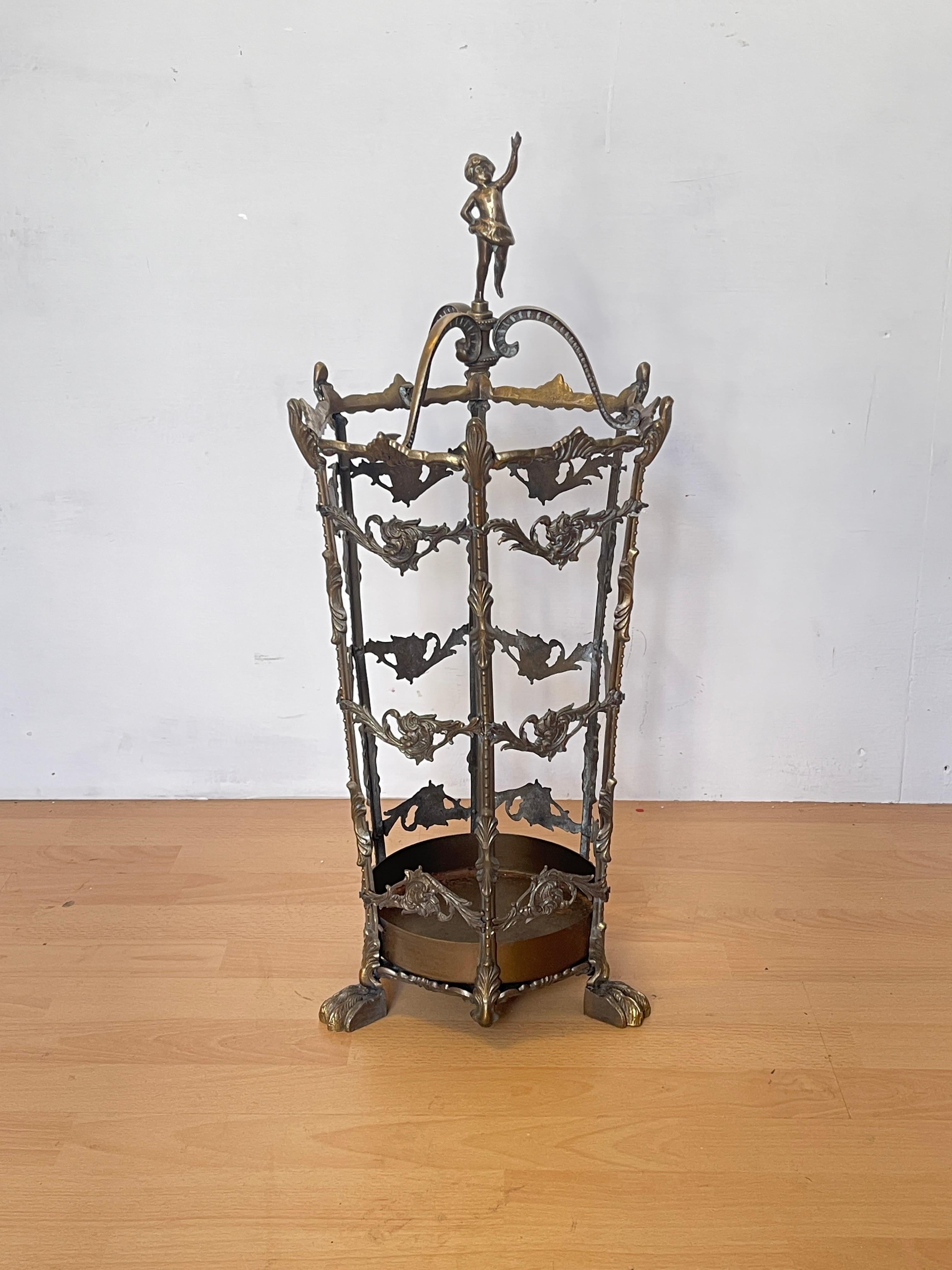 Fine period umbrella stand made of solid brass, embellished with floral decorations and leaf motifs worked in relief.
The structure features a dancing female figure on top and lion's paw feet, details reminiscent of the Art Nouveau/Victorian style.