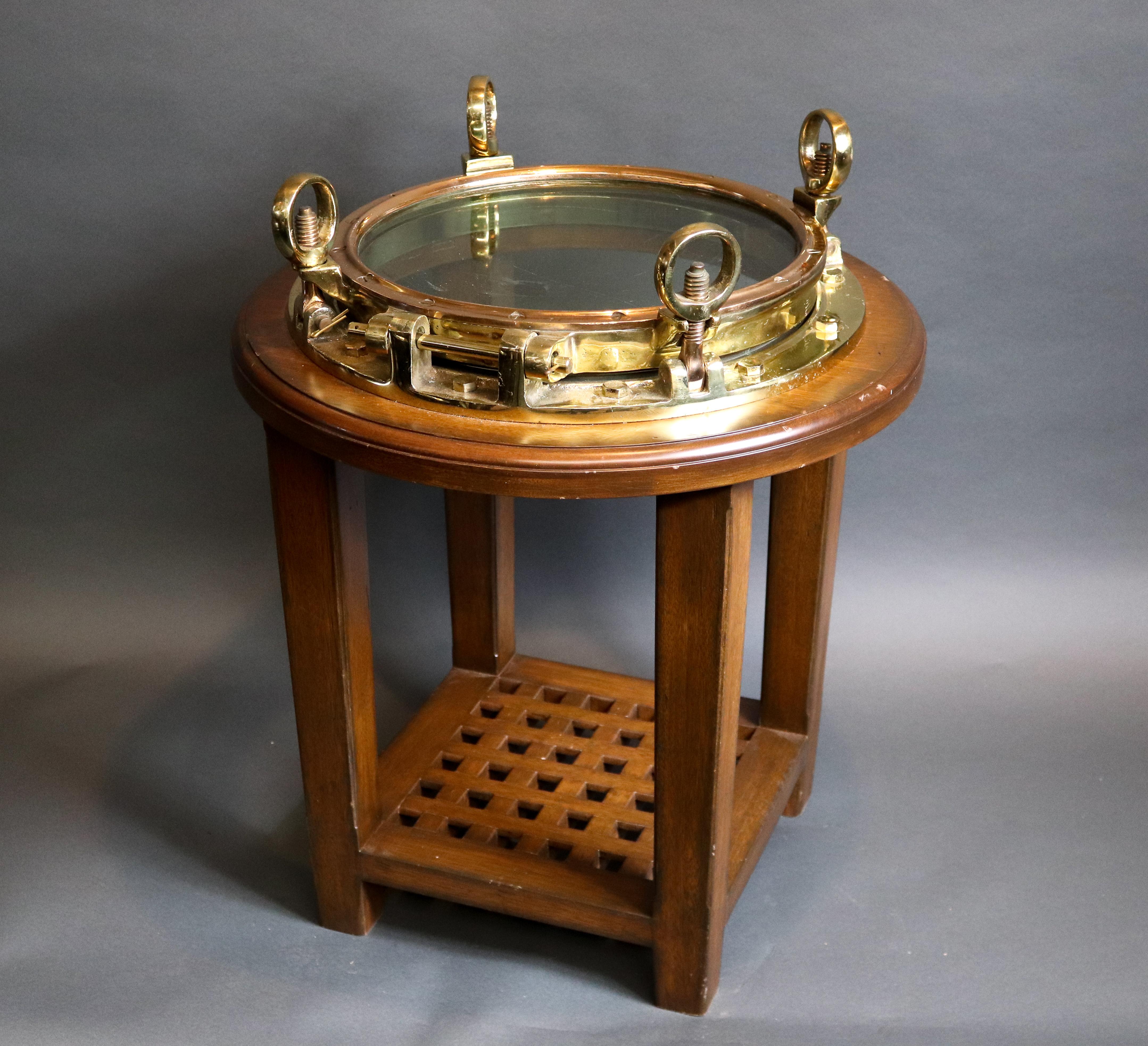Quality polished brass ships porthole that has been fitted to a custom mahogany table with a shelf with the form of a ships granting. Weight is 80 lbs. 26