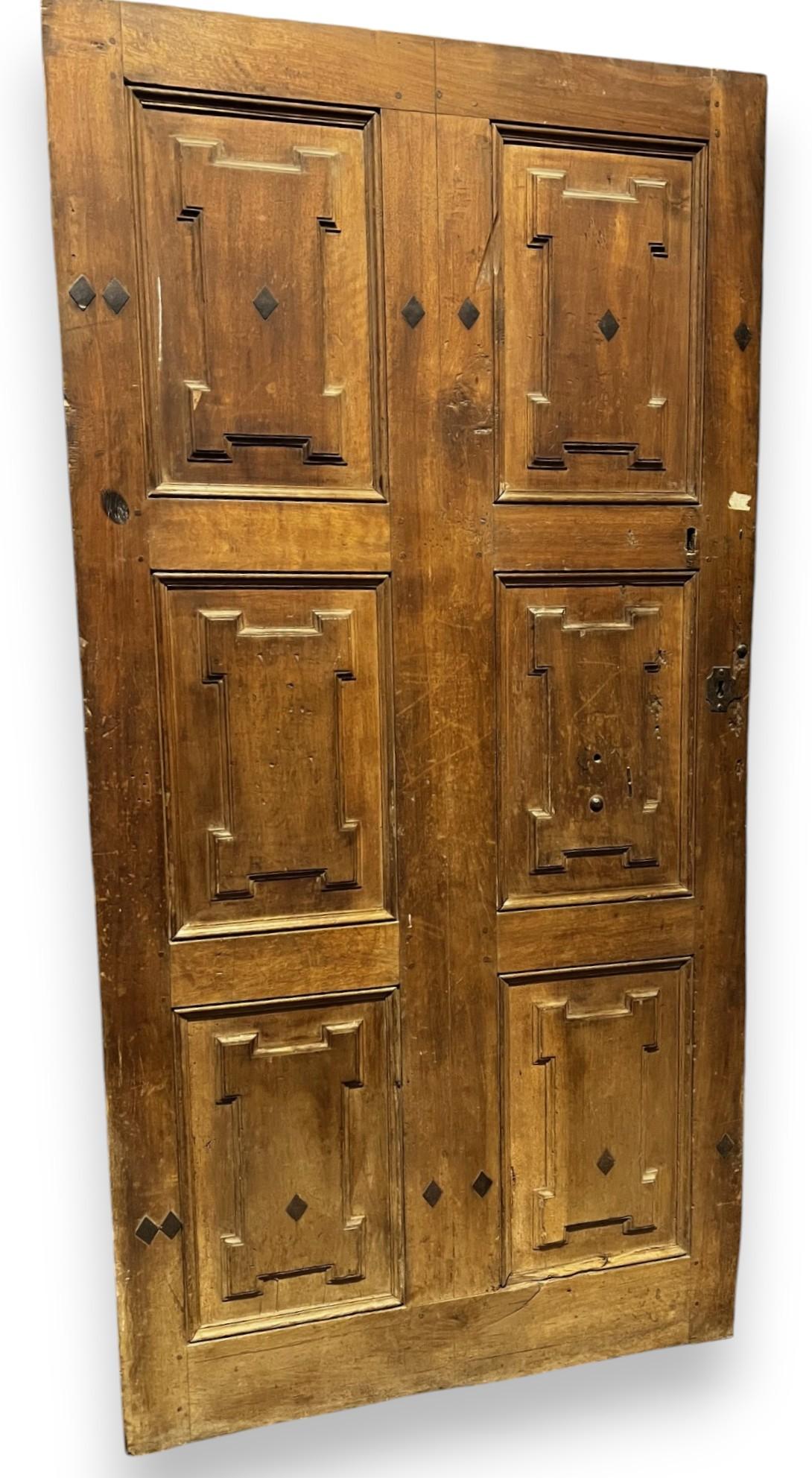 Antique One-Wing Walnut Entrance Door (originated with two doors but has been joined). The panels are carved in geometric decorations with frets and has nails at the top and bottom. Original from the Eighteenth Century, The back is smooth, The