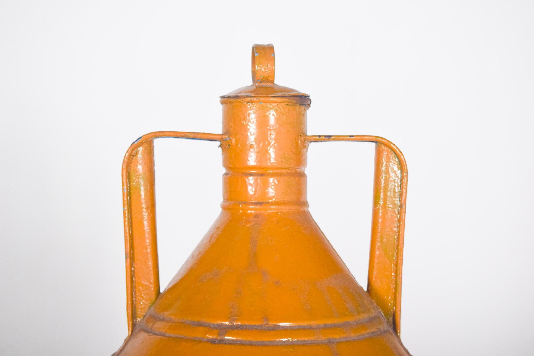 Récipient métallique traditionnellement utilisé pour stocker et transporter l'huile d'olive ou d'autres liquides. De forme cylindrique, avec un corps robuste et un sommet effilé qui mène à une bouche étroite, fermée par un bouchon en métal.
Il est