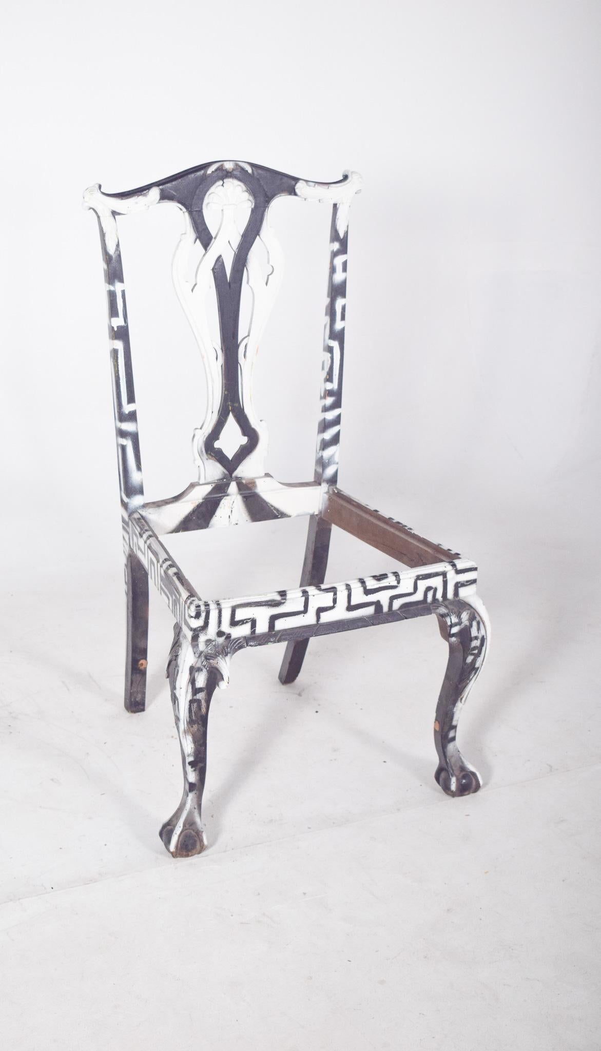Chaise de salle à manger peinte en noir et blanc. Réinterprétée avec une intervention artistique contemporaine qui transforme radicalement son aspect d'origine. La structure, avec son dossier découpé et ses pieds avant en forme de griffe, a reçu une