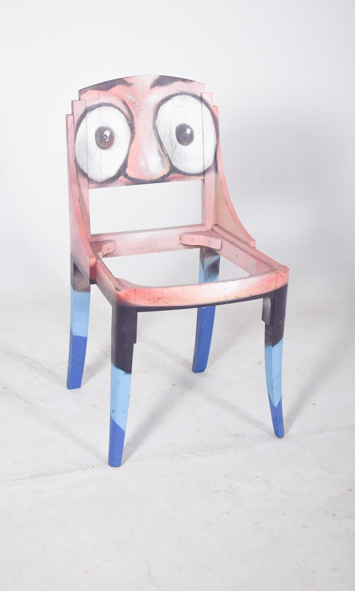 Silla de comedor pintada. Reinterpretado con intervención artística contemporánea, transformando un objeto funcional en una pieza de arte urbano. El respaldo, de líneas curvas y elegantes, presenta una pintura con expresivos ojos saltones sobre un