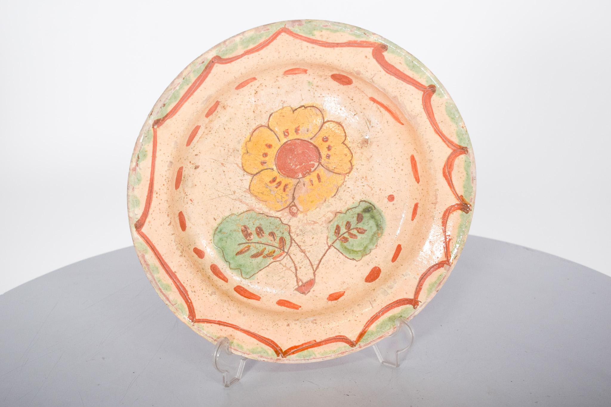 Plaque d'argile peinte et émaillée. Décor polychrome avec des fleurs, peint à la main, caractéristique de la tradition artisanale. La surface présente un fond beige clair, avec un motif floral central, où une fleur jaune avec un cœur rougeâtre est