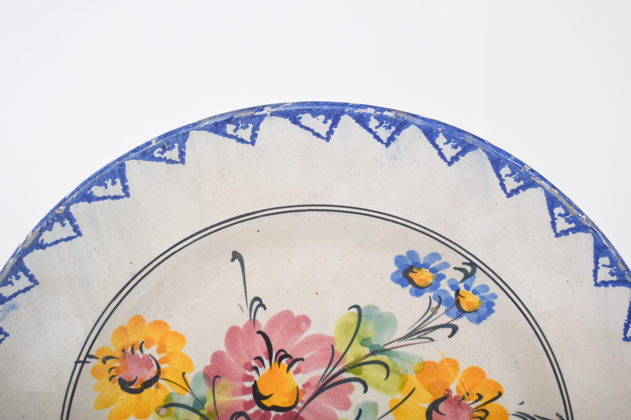 Piatto di terracotta portoghese. Decorazione policroma con motivi floreali e geometrici. Al centro c'è un bouquet di fiori nei toni del giallo, del rosa e del blu, accompagnati da foglie verde chiaro, che mostrano un aspetto tradizionale e